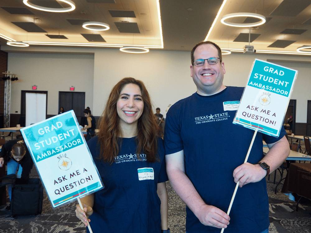 four students sit at a table and hold up artwork they drew for the camera