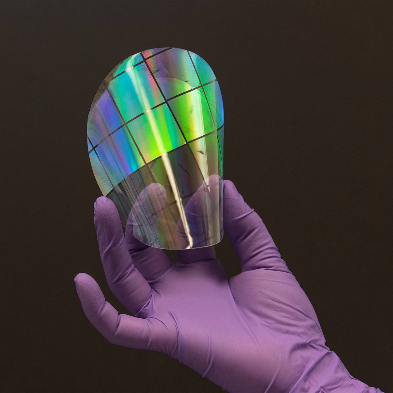 A purple, gloved hand holds an iridescent chip against a dark background
