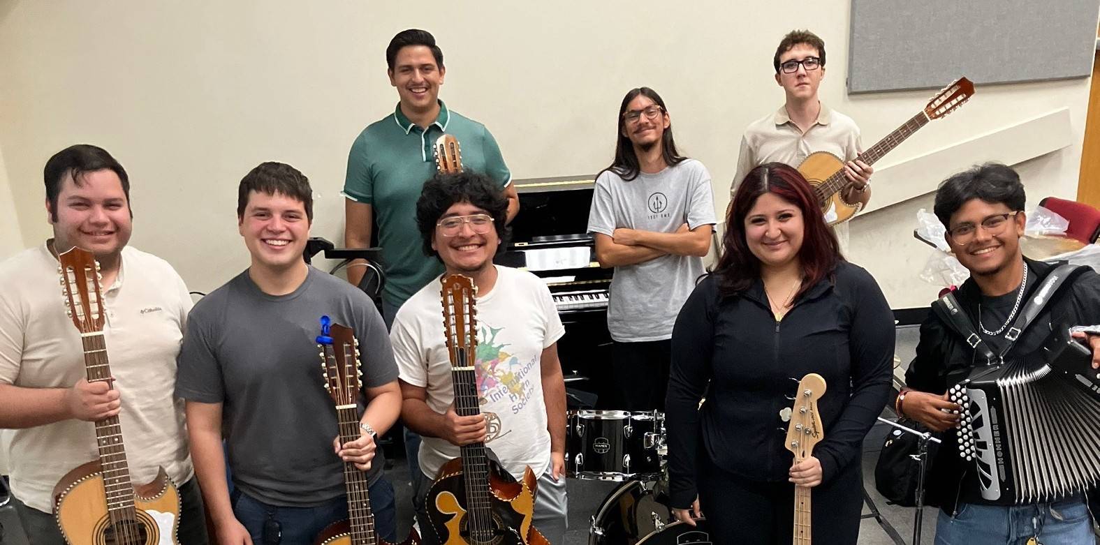 Students stand in a classroom, smiling and holding instruments.