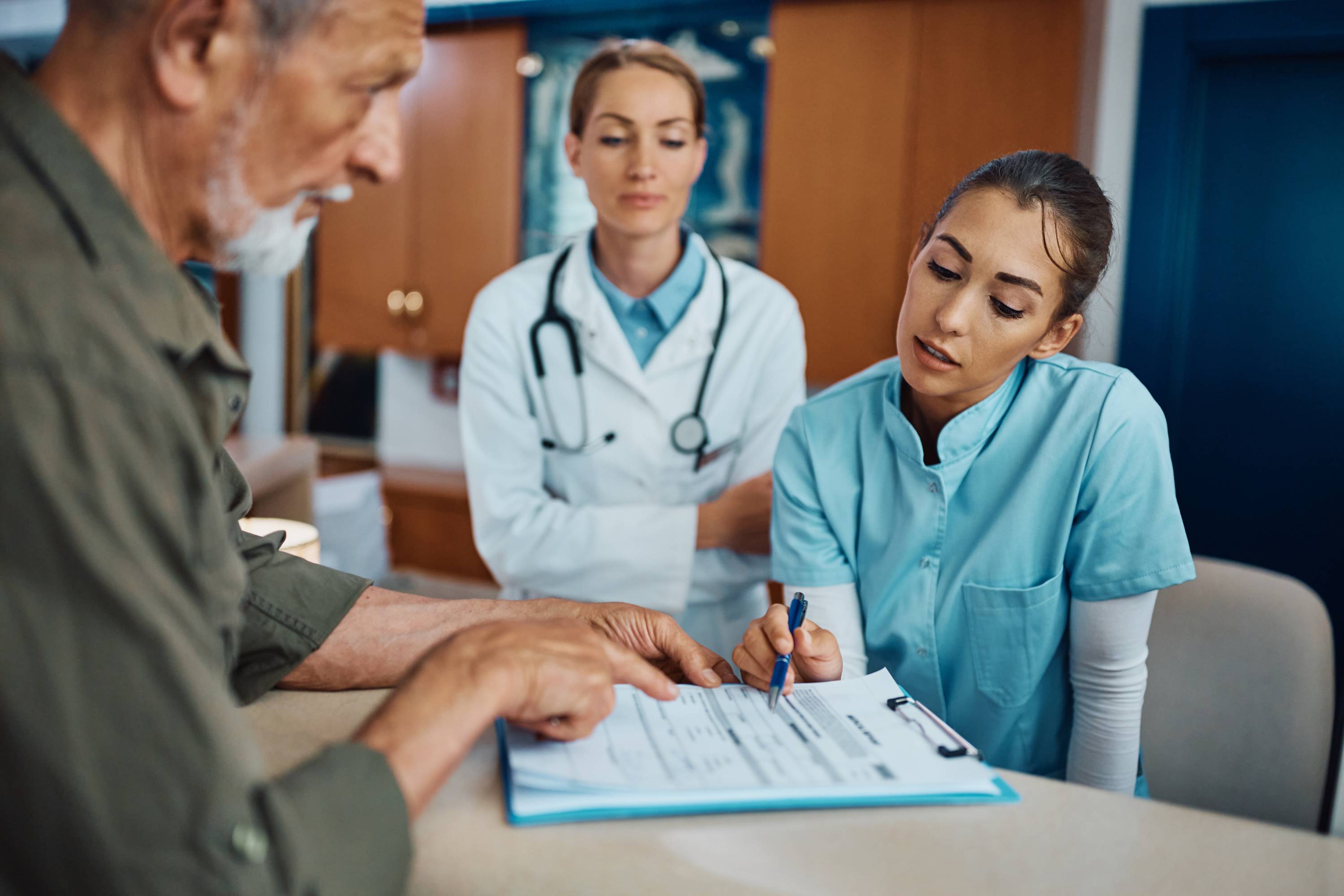 a medical assistant helping a patient with a doctor looking on in the background 