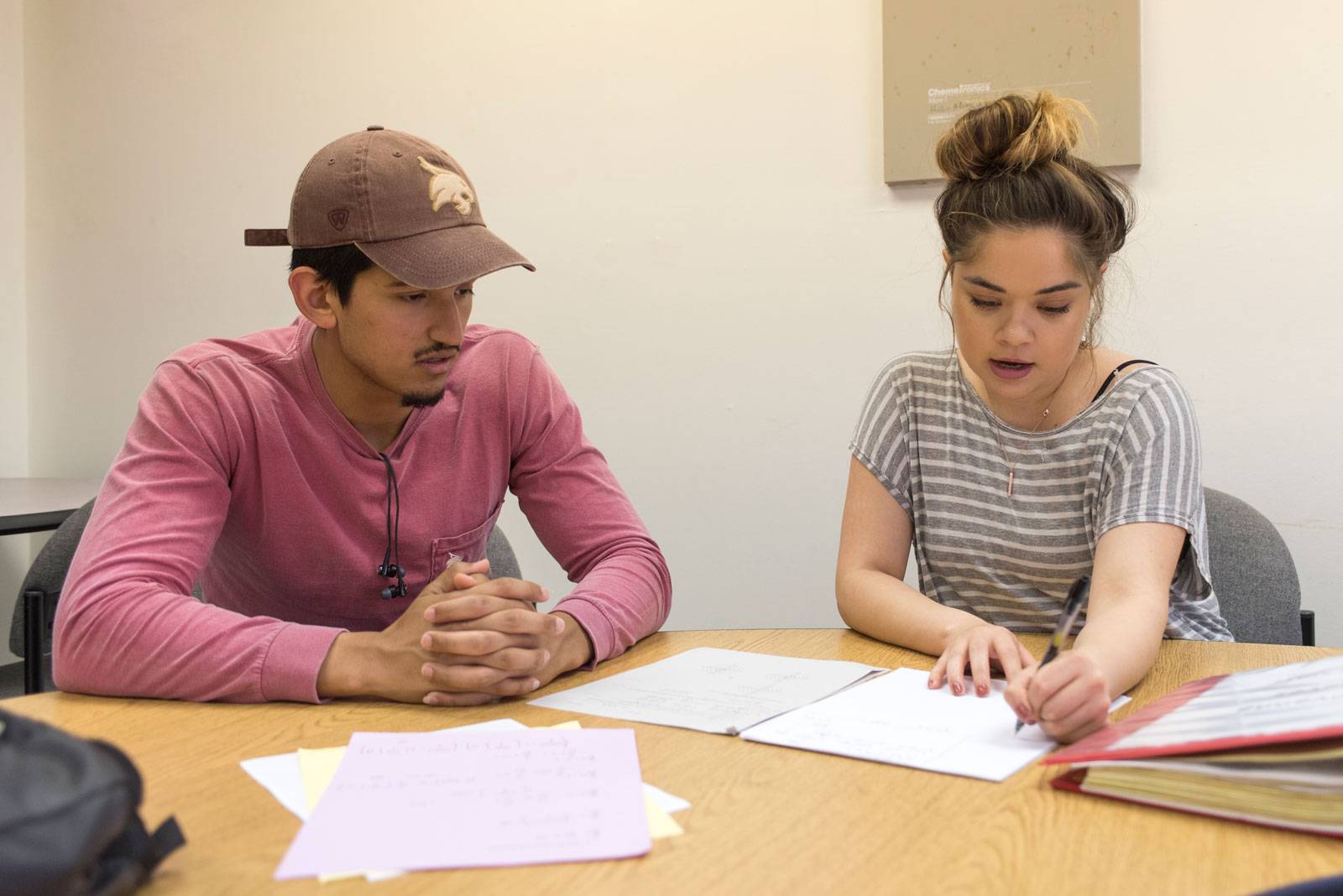 two hispanic students looking at papers on desk 