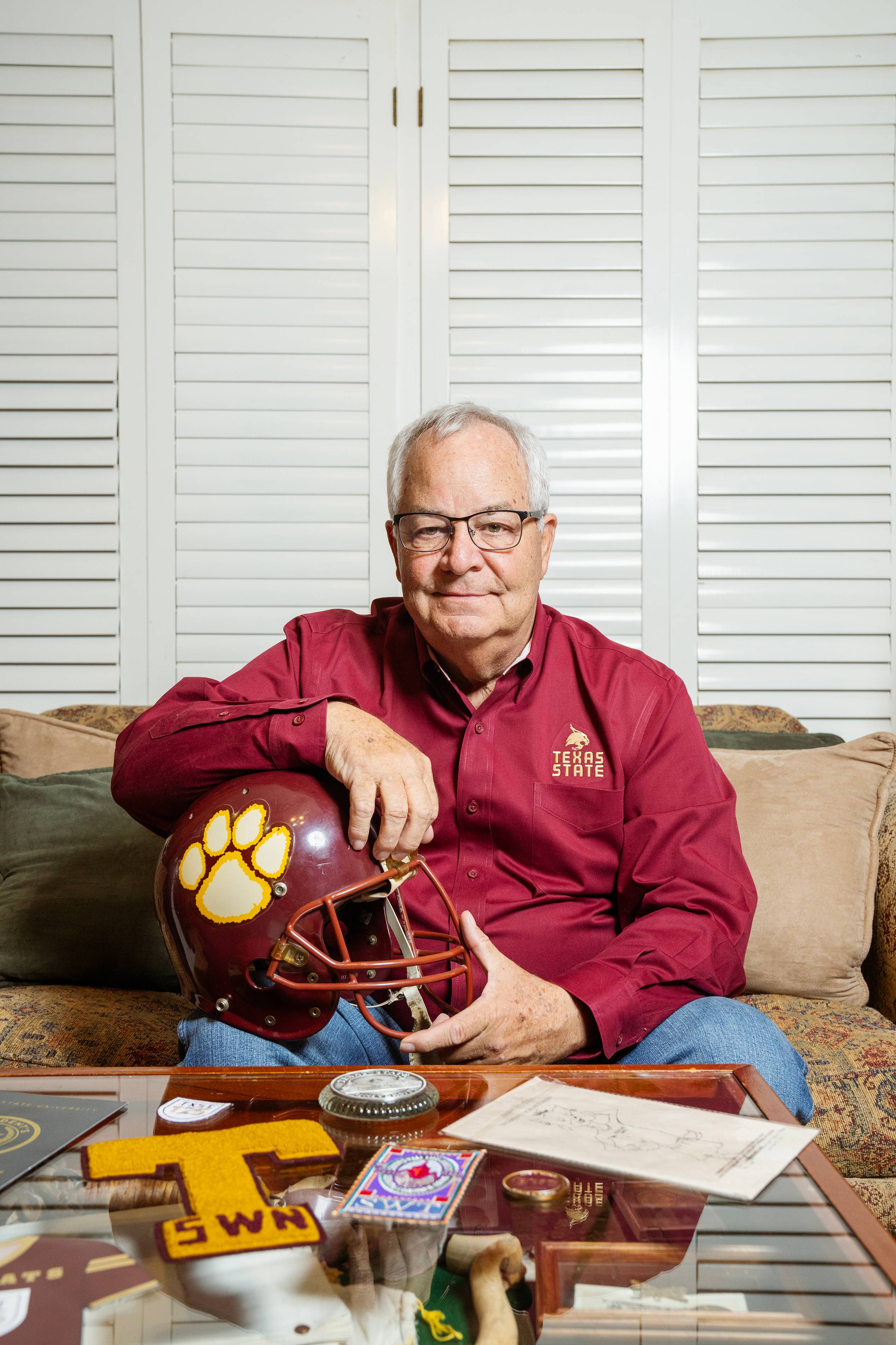 Tom Madden sits on a couch while holding a maroon football helmet on his lap