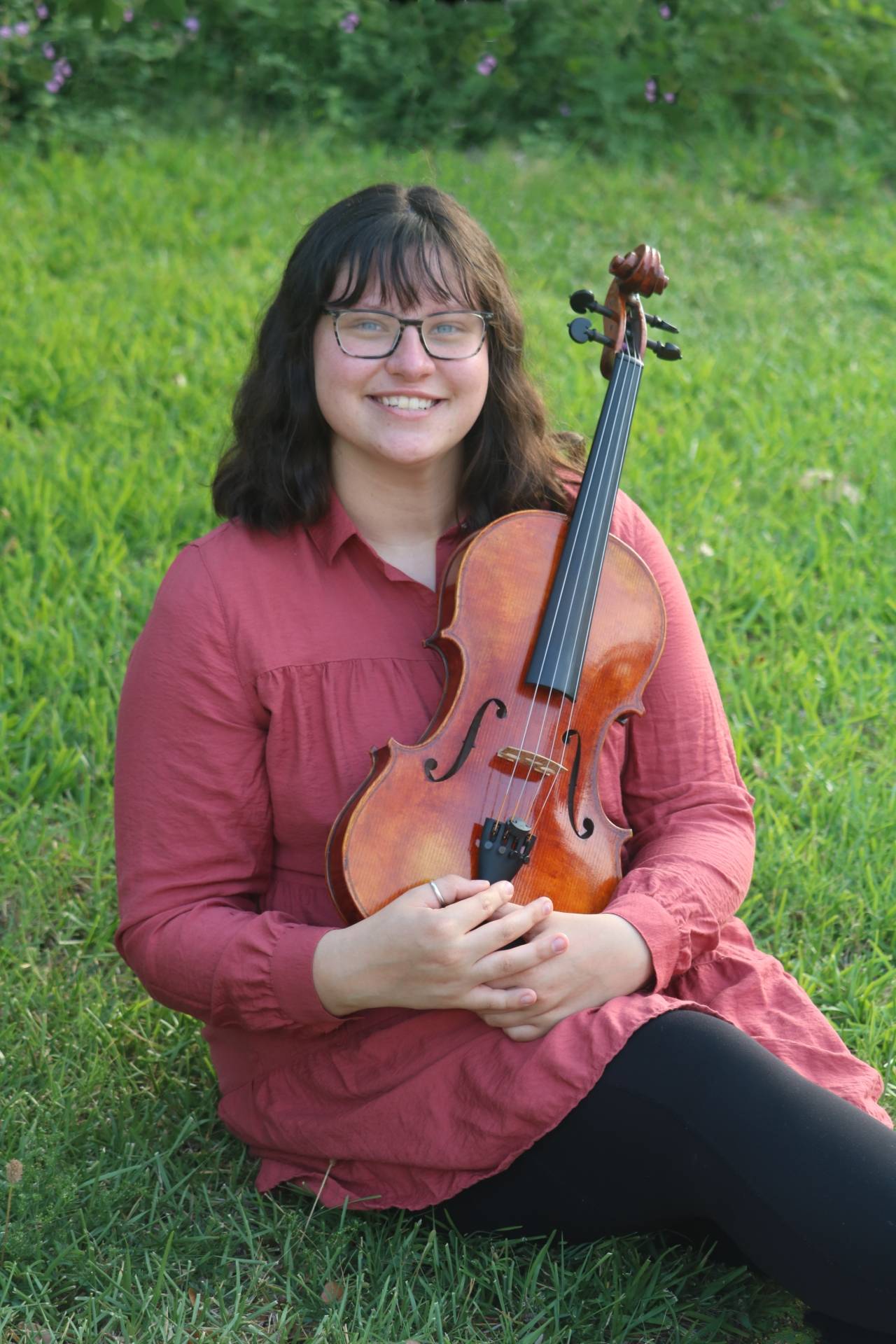 Student holding violin sitting on grass