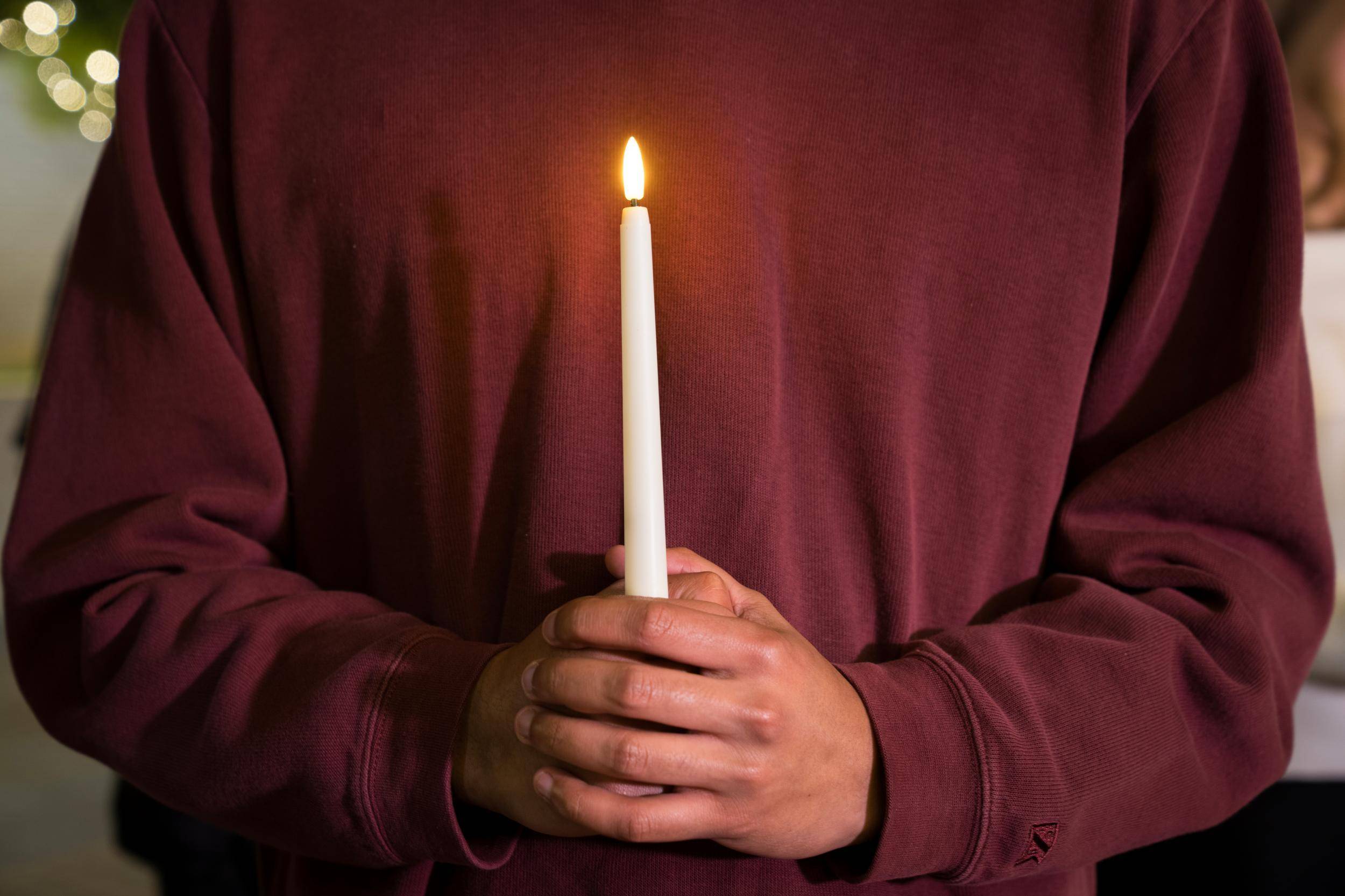 man in maroon sweater holding up a single white taper candle