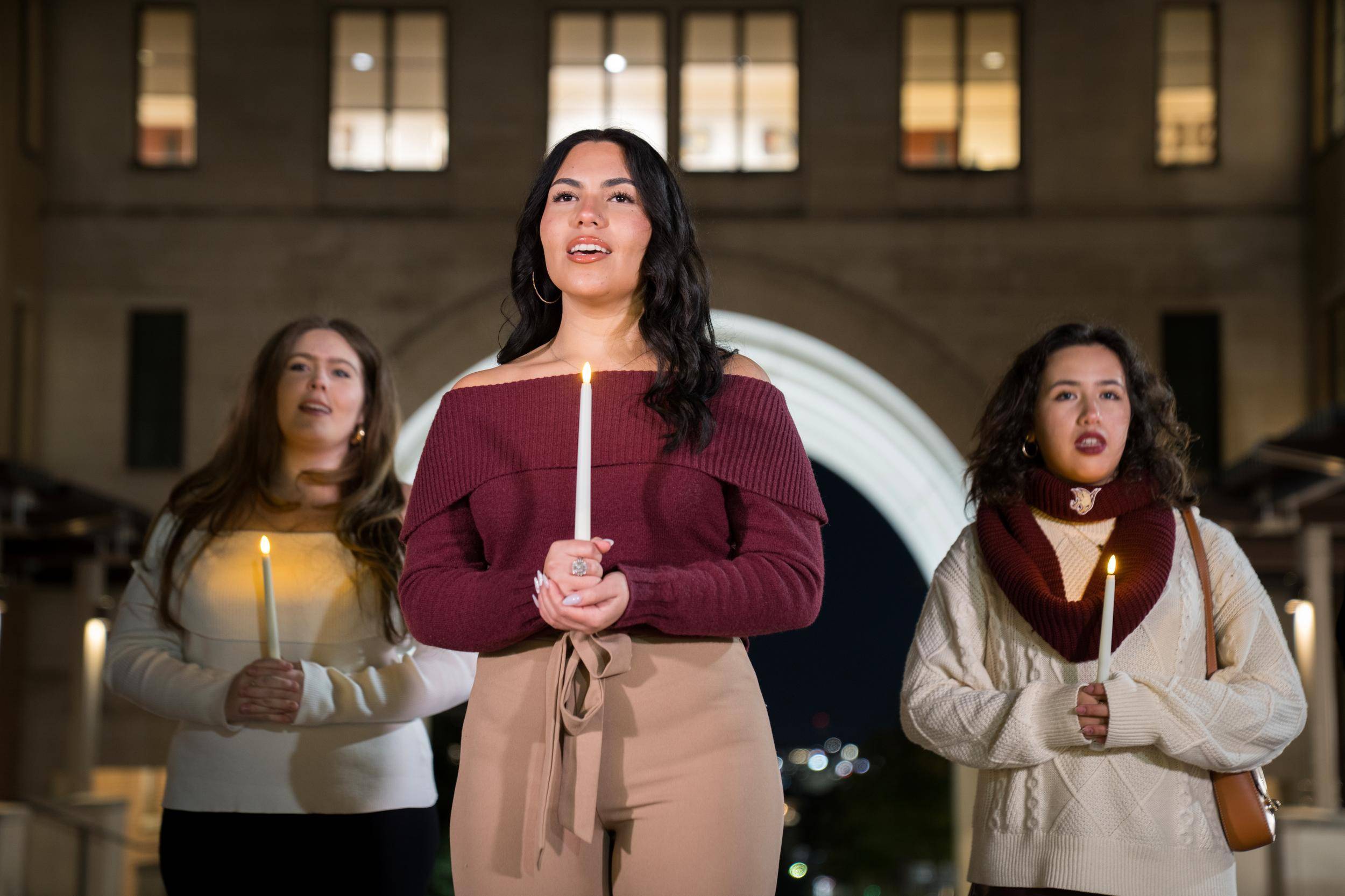 holiday video of students singing while walking around campus and holding white taper candles