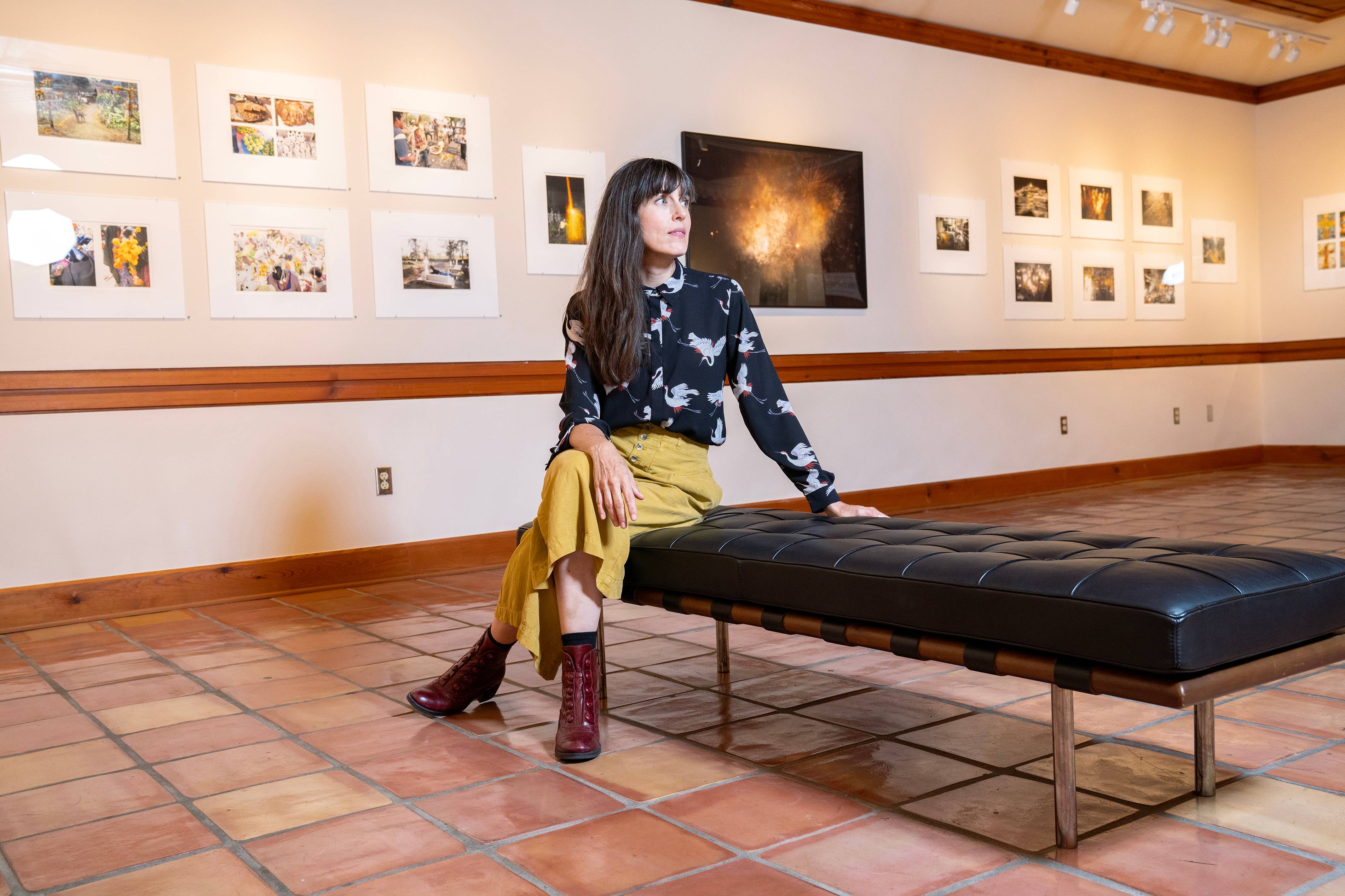 carrie fountain sits on a leather bench in a large art gallery. she is looking off to the left