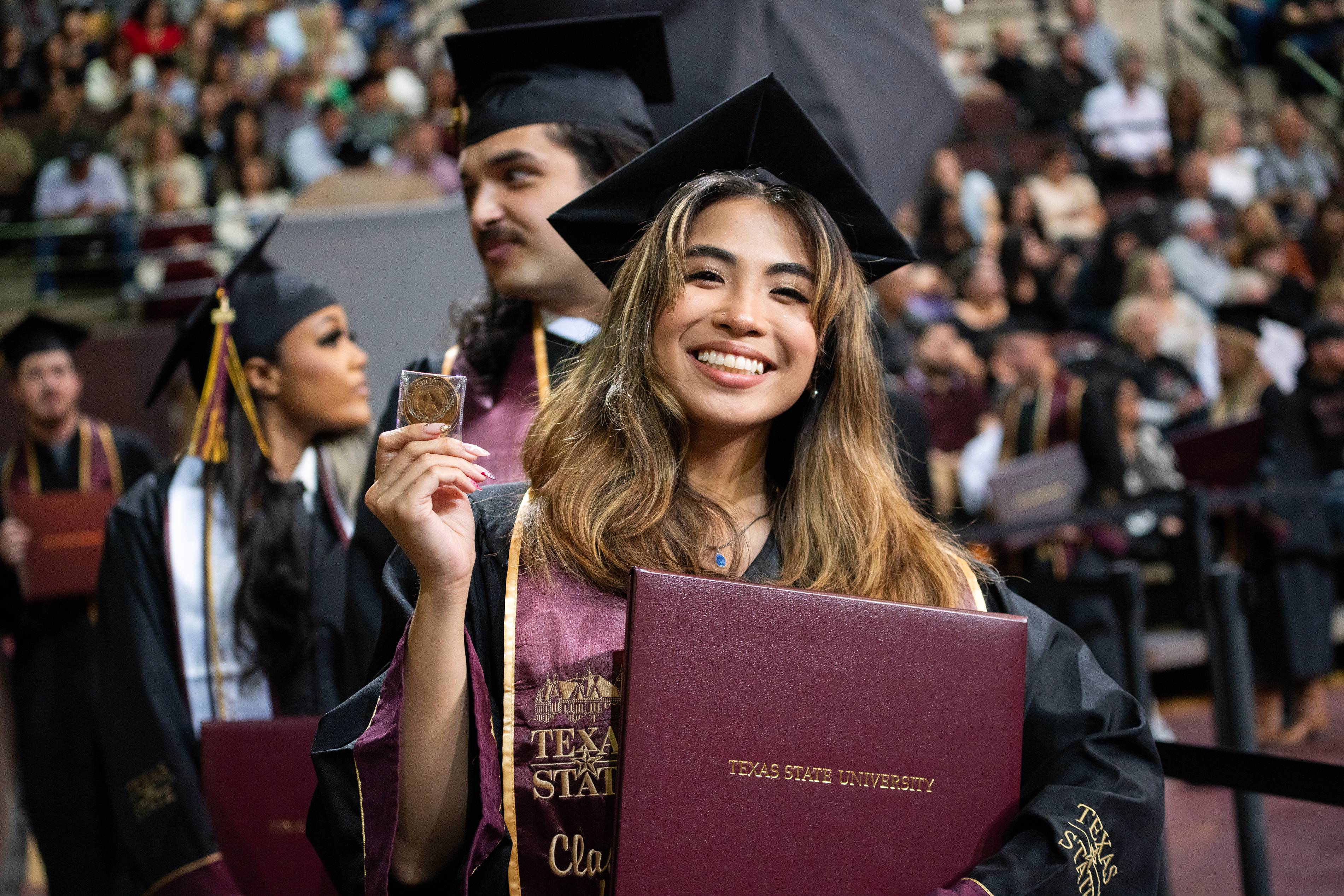 female graduate holding up gold challenge coin