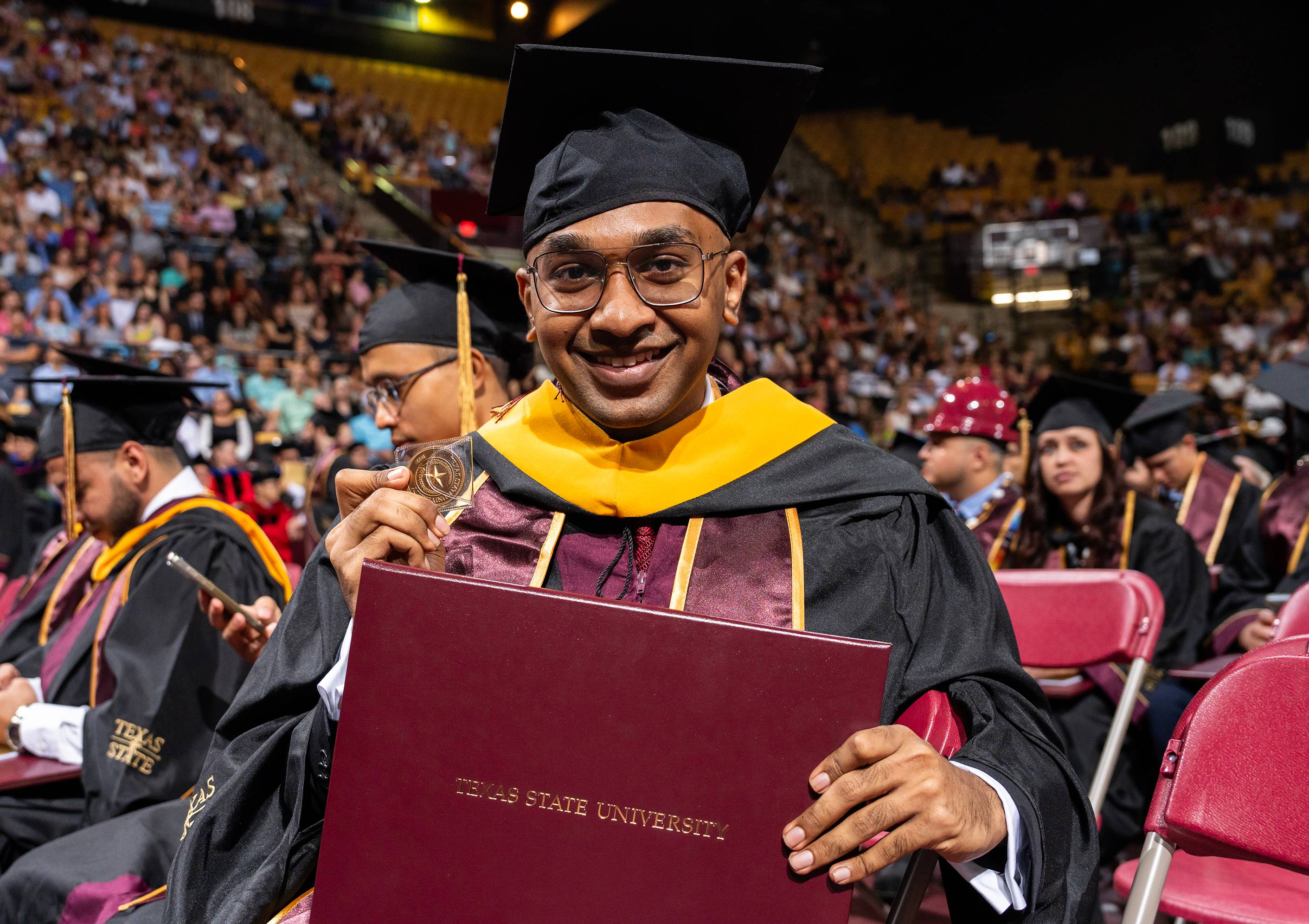 male graduate holding up gold challenge coin