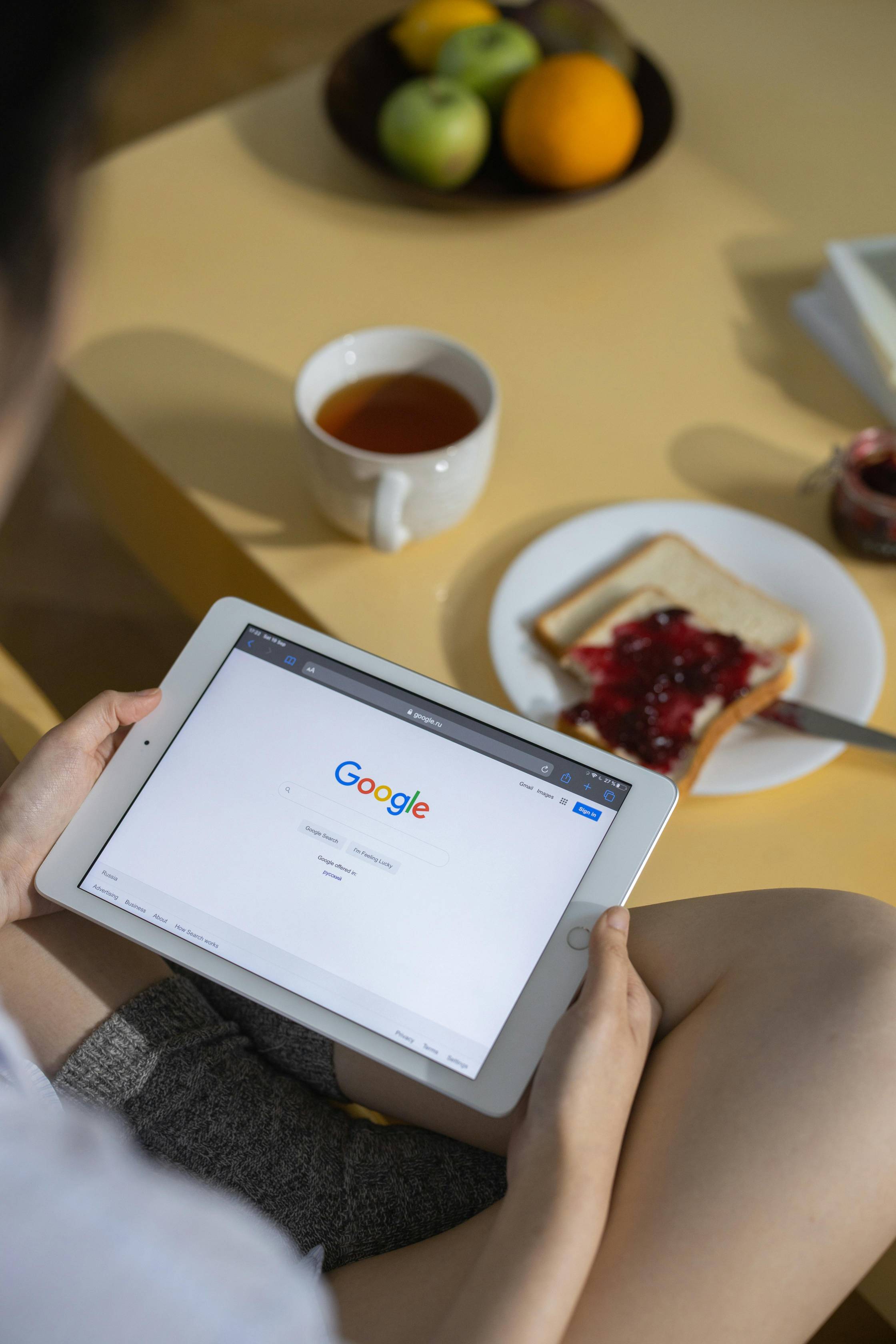 Person using a tablet displaying the Google homepage while seated at a table with breakfast and tea. The image represents online search, digital marketing, customer engagement, and managing a business’s online presence, making it ideal for a workshop on Google Reviews, reputation management, and local SEO.