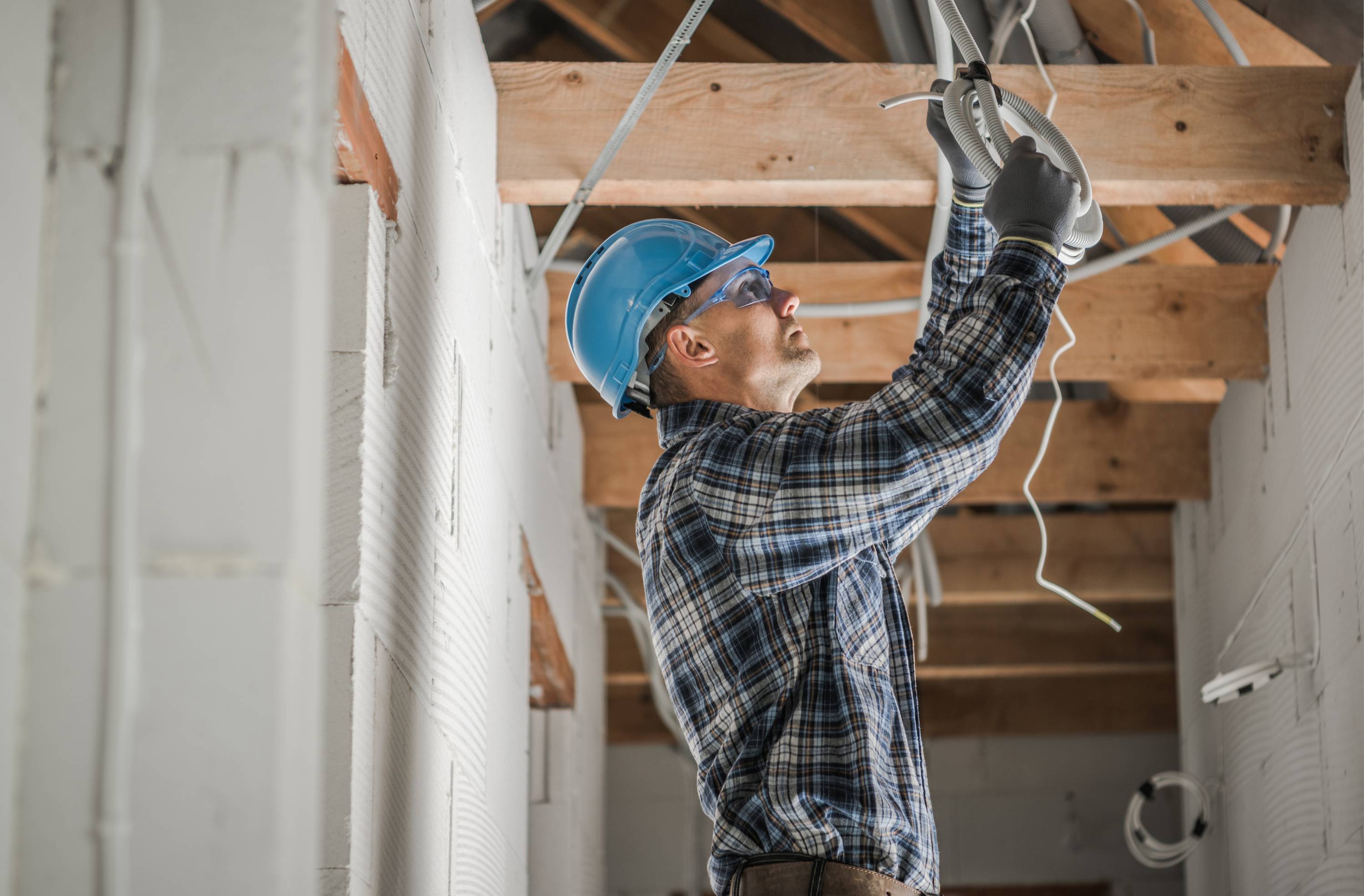 an electrician in hard hat working on wires above him