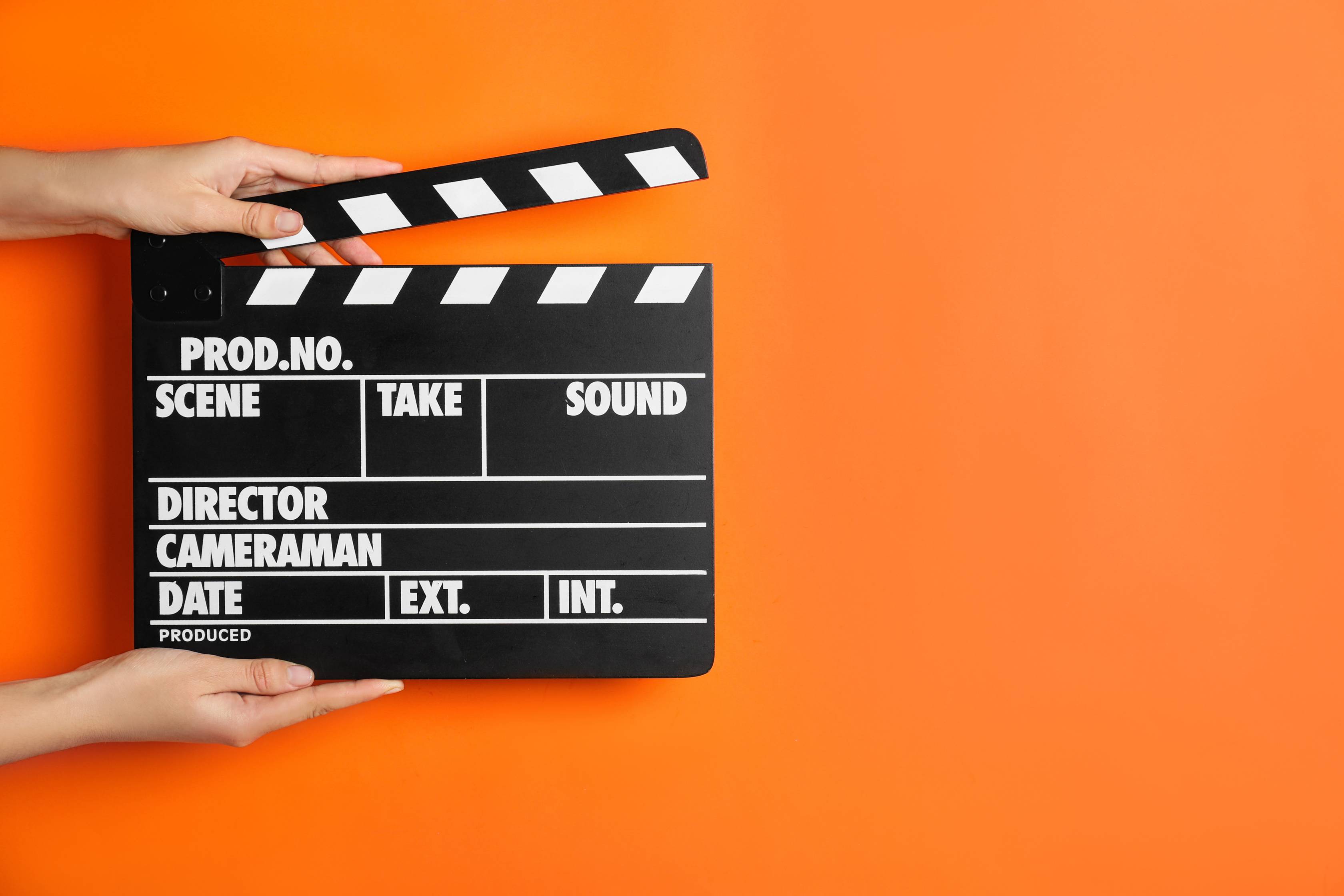 two hands holding a film clapper against an orange background