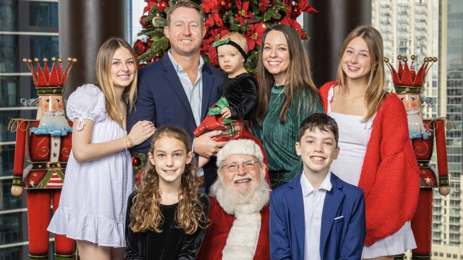family dressed in holiday attire posing for photo with Santa Claus