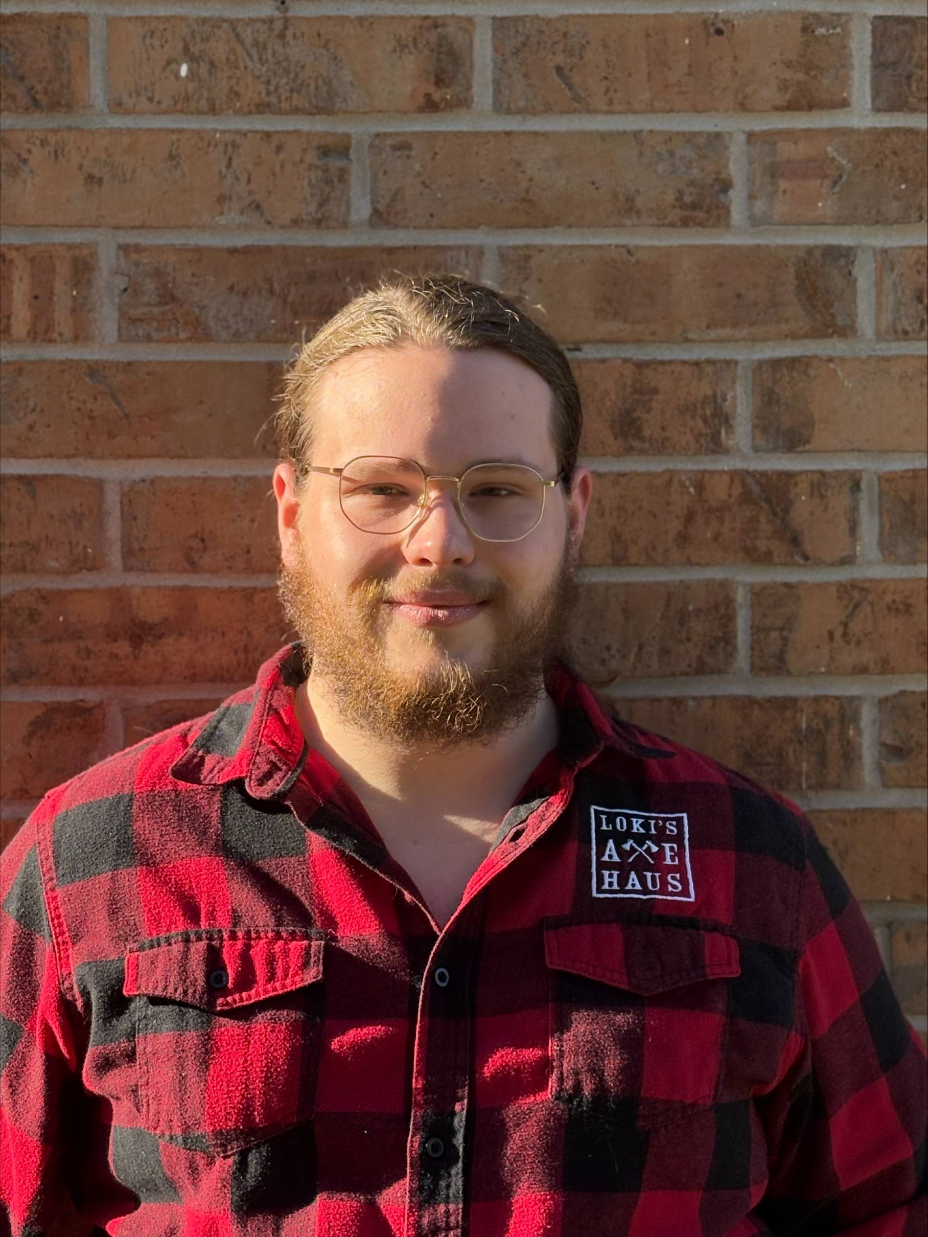 man with glasses and beard, plaid shirt, against brick wall