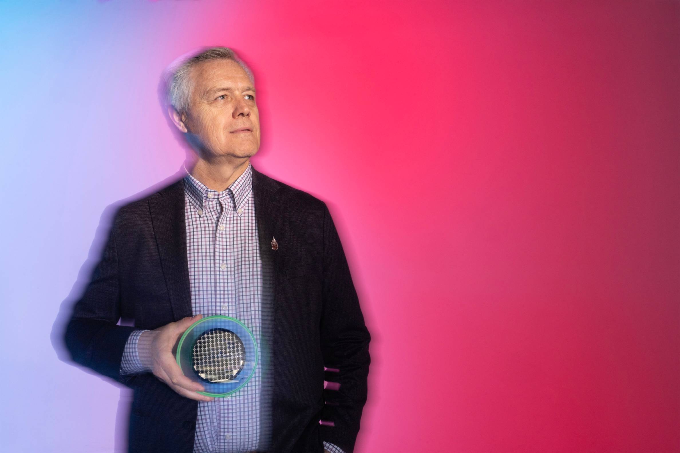 man holding semiconductor in front or blue to pink gradient wall
