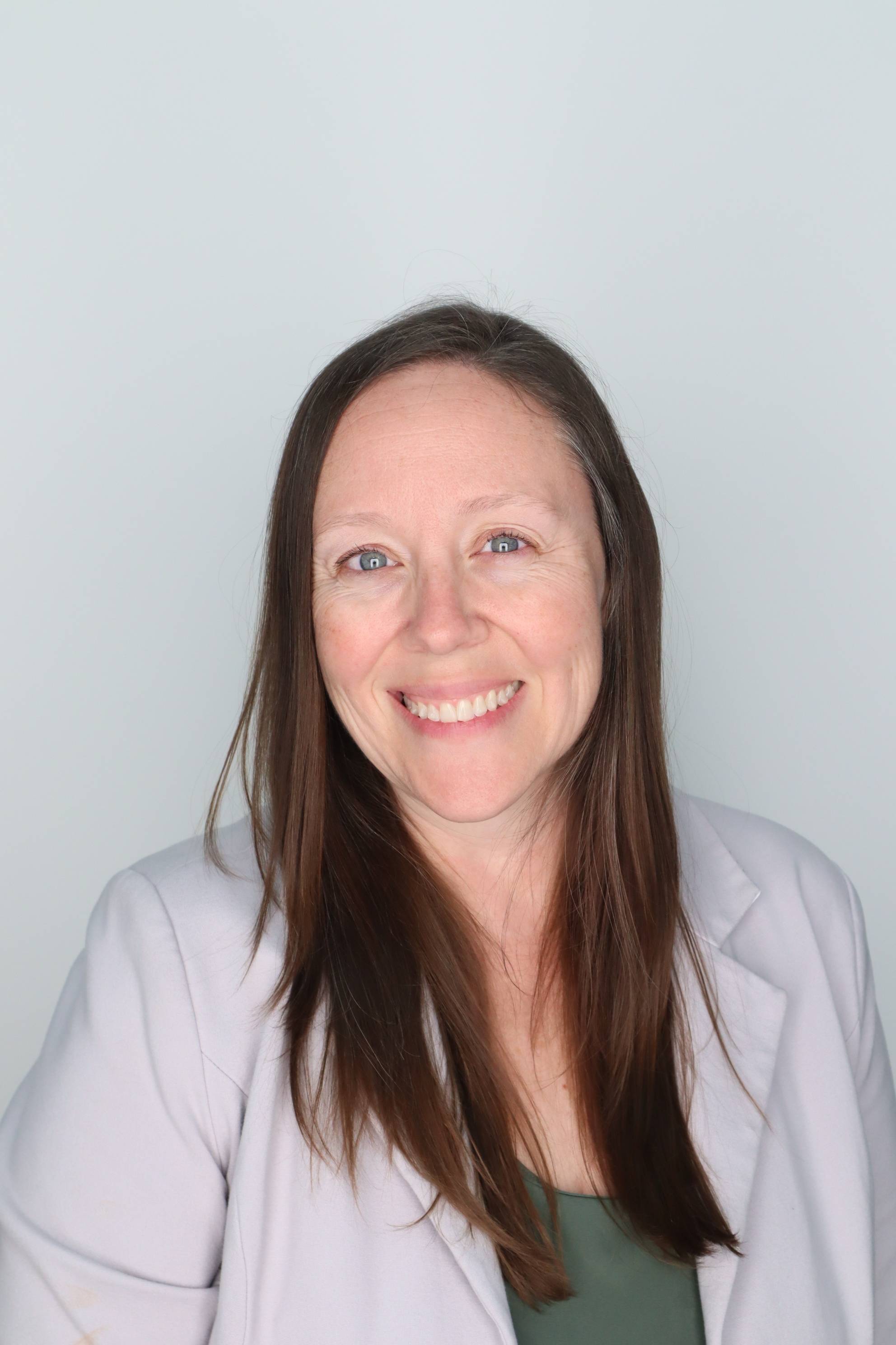 White woman with blonde hair smiling and standing next to a stair case