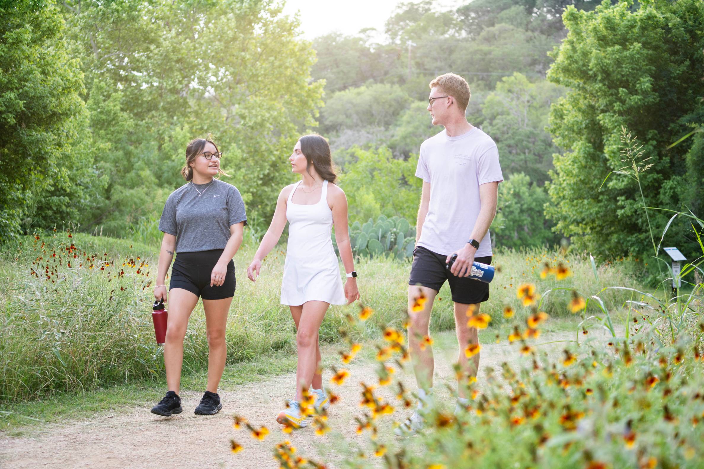 two women and one male hiking on green trail