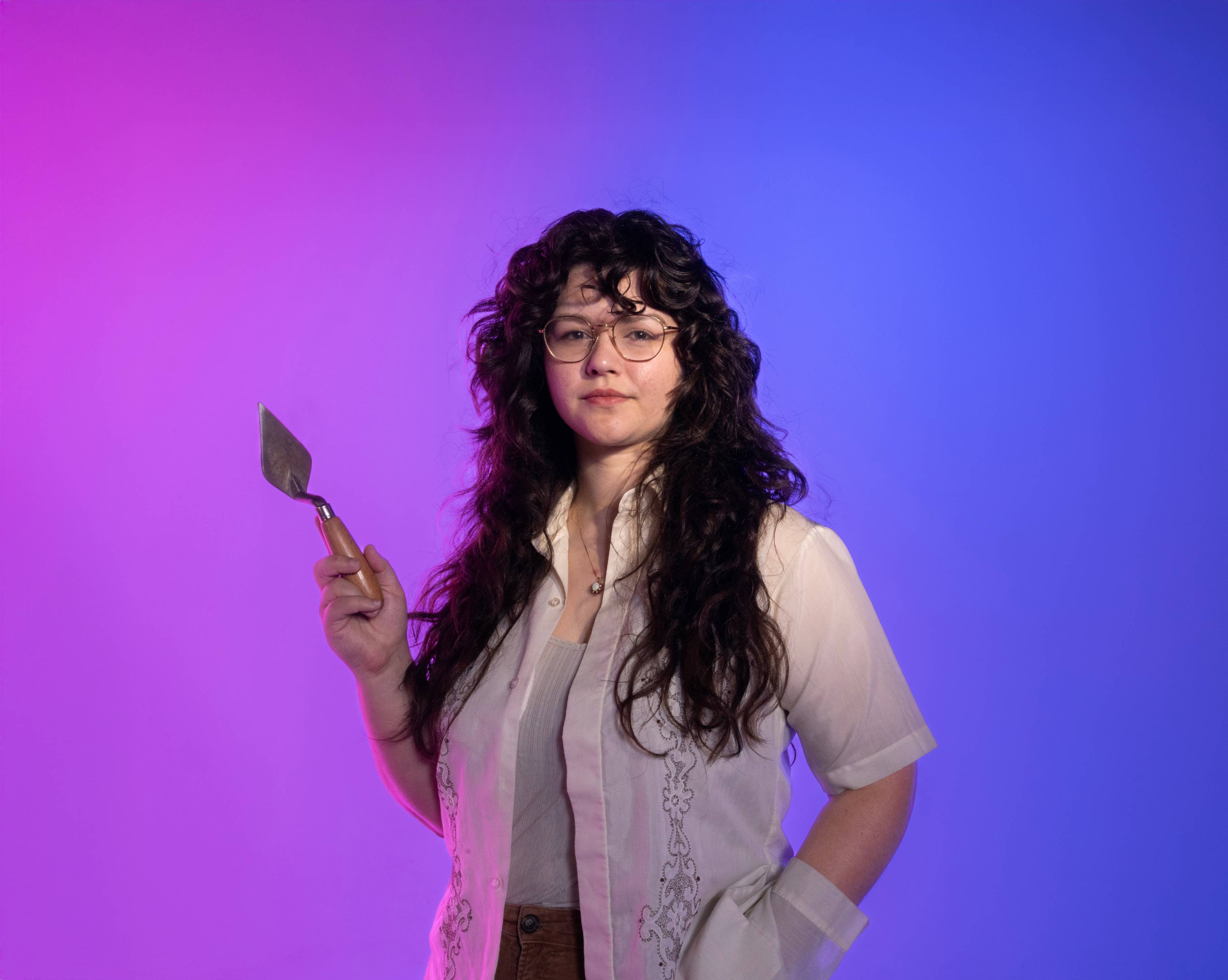 Erin Mathison stands in front of a purple to blue gradient background while holding a metal trowel in her right hand