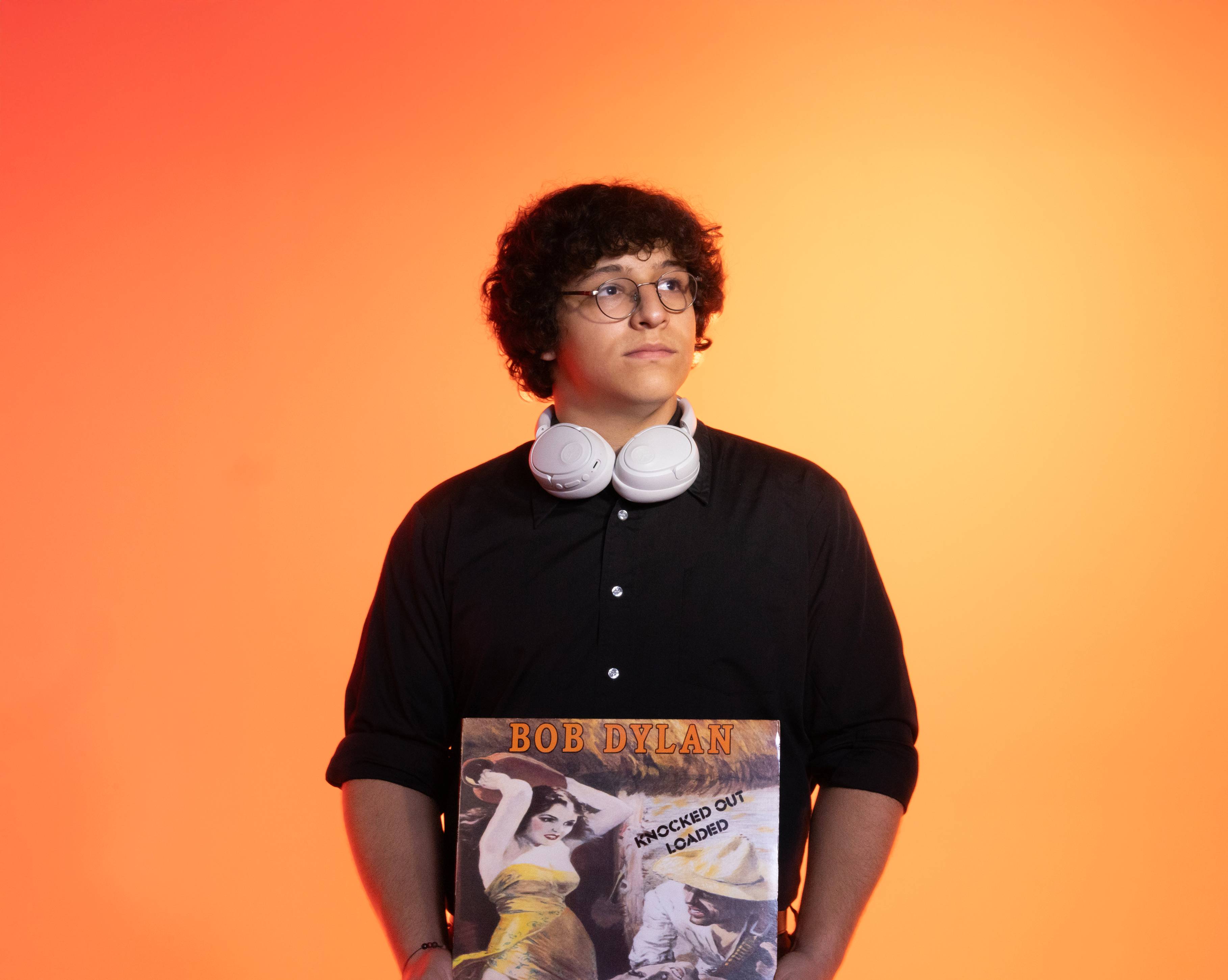 Mason Moreno holds a Bob Dylan vinyl while standing in front of orange and yellow gradient background
