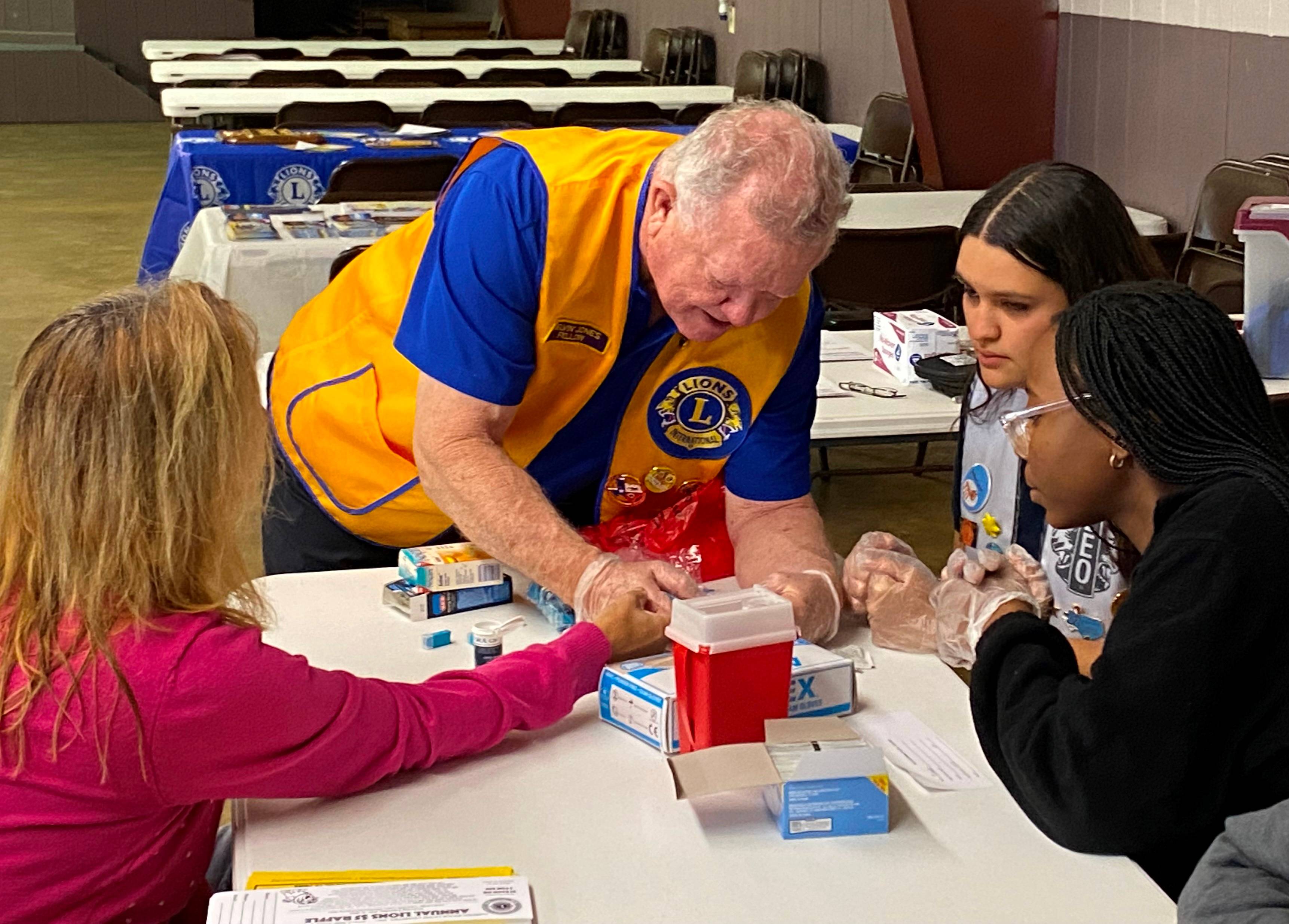 man teaches two women how to perform blood sugar testing on another woman