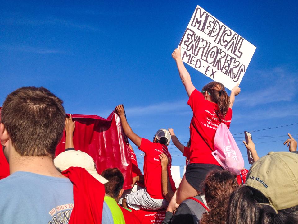 woman sitting on shoulders of another person holding up sign that reads "Medical Explorers"
