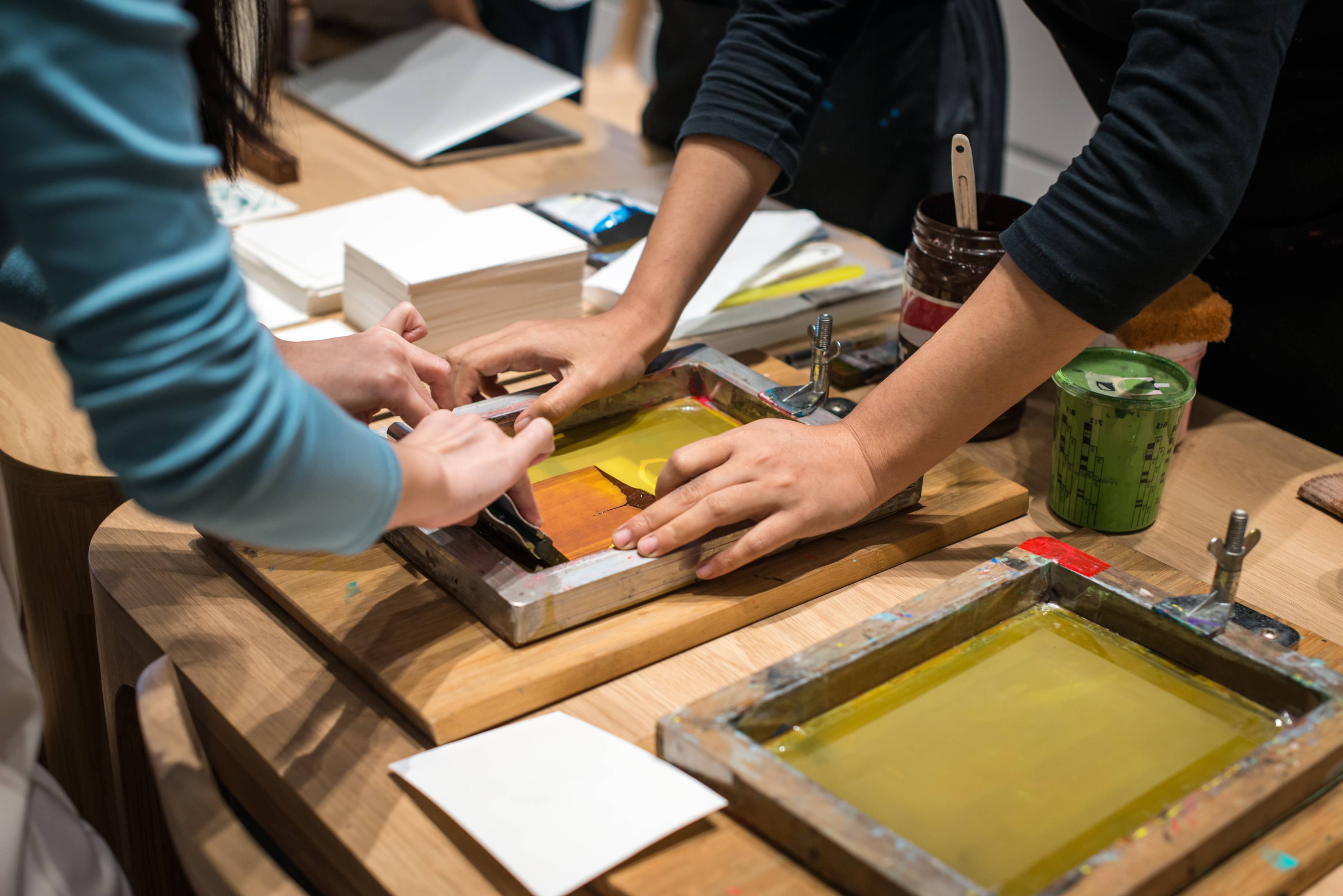 Two sets of hands working simultaneously on a screen print.