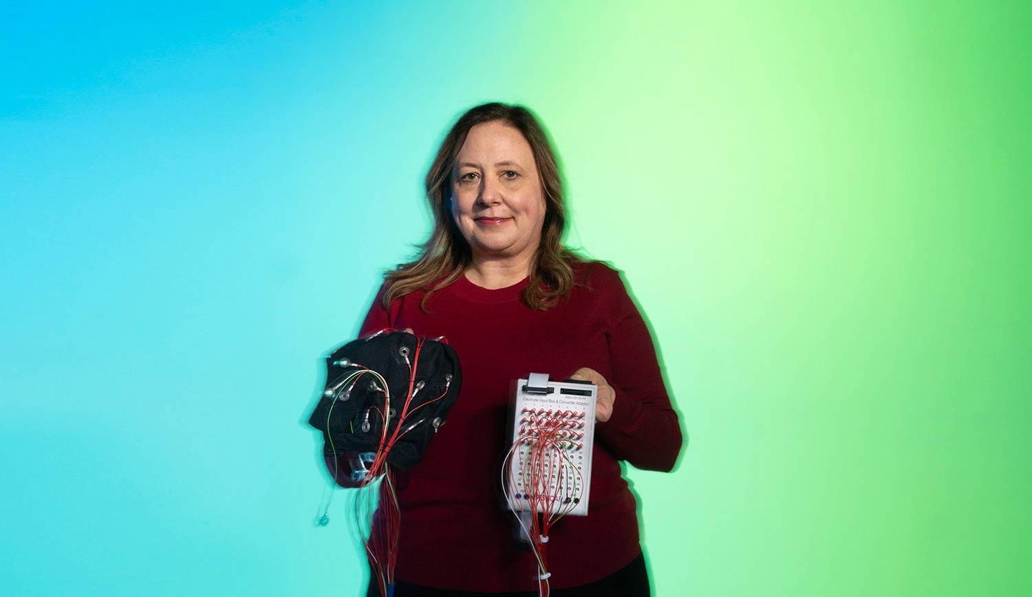 Dr. Carmen Westerberg holds a medical device in her hands while standing in front of a blue and green gradient background