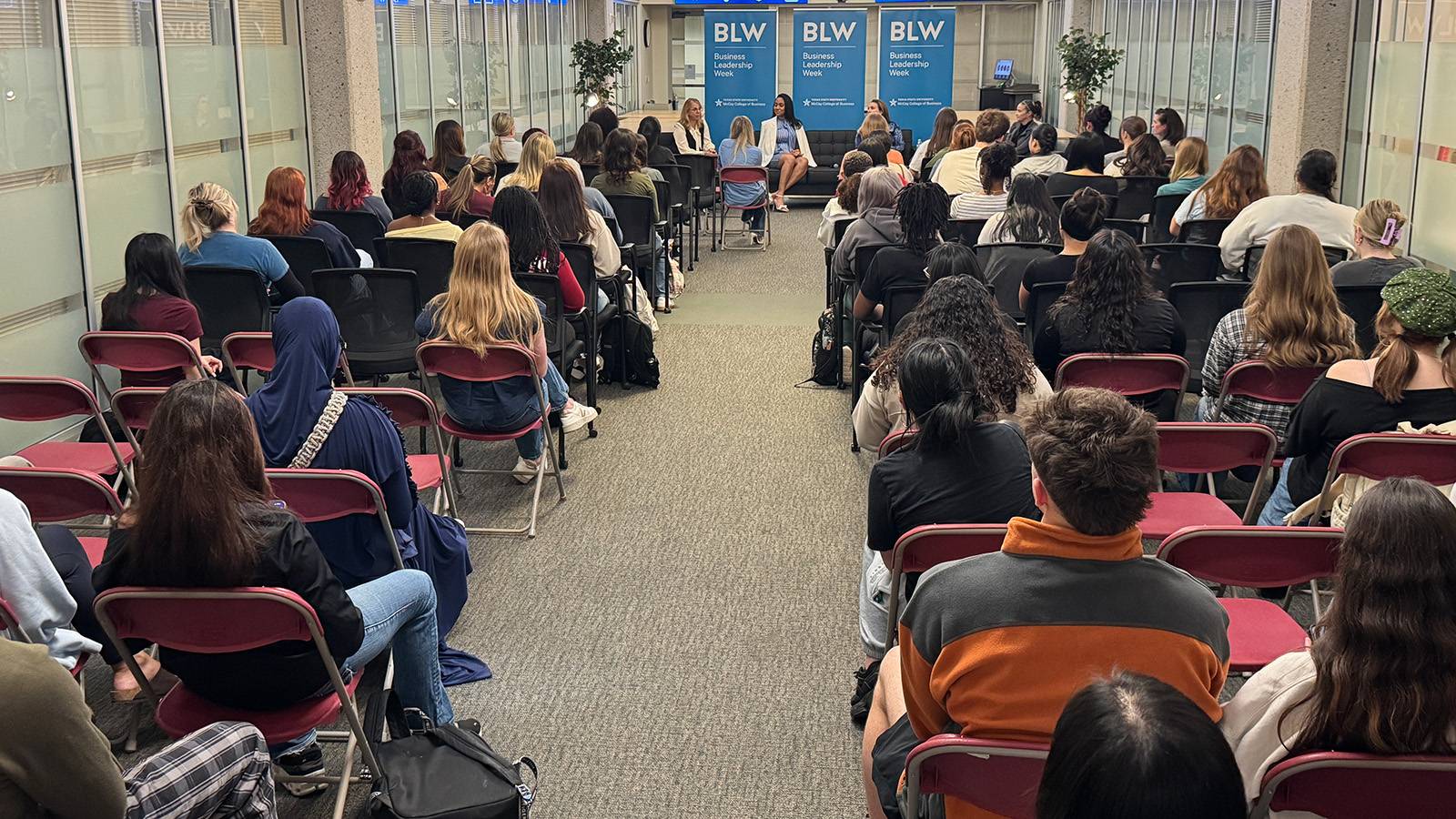back view of group of students sitting in chairs looking ahead at speakers during a panel session