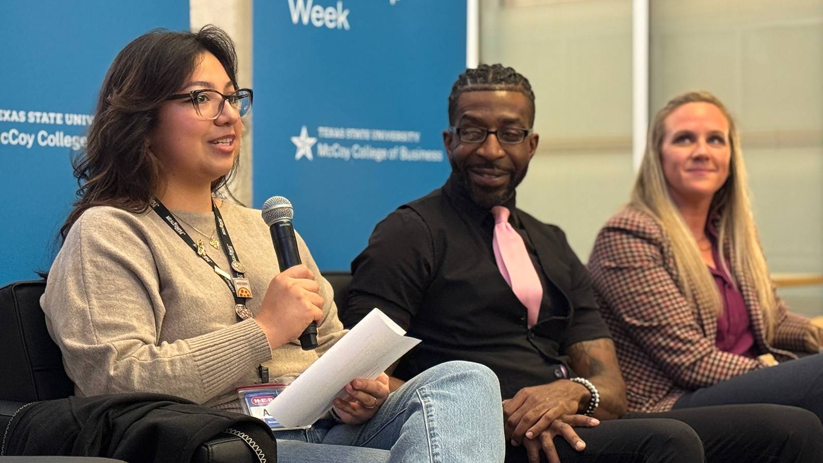 three people sitting on a couch during a panel session while a women speaks into a microphone and the other two look on