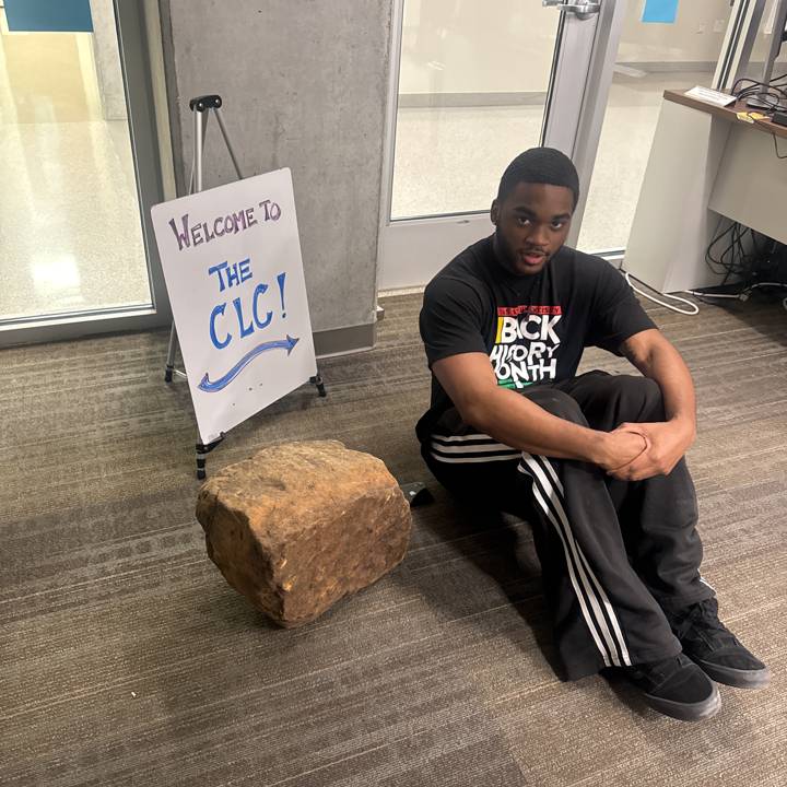 a boy sitting next to a rock