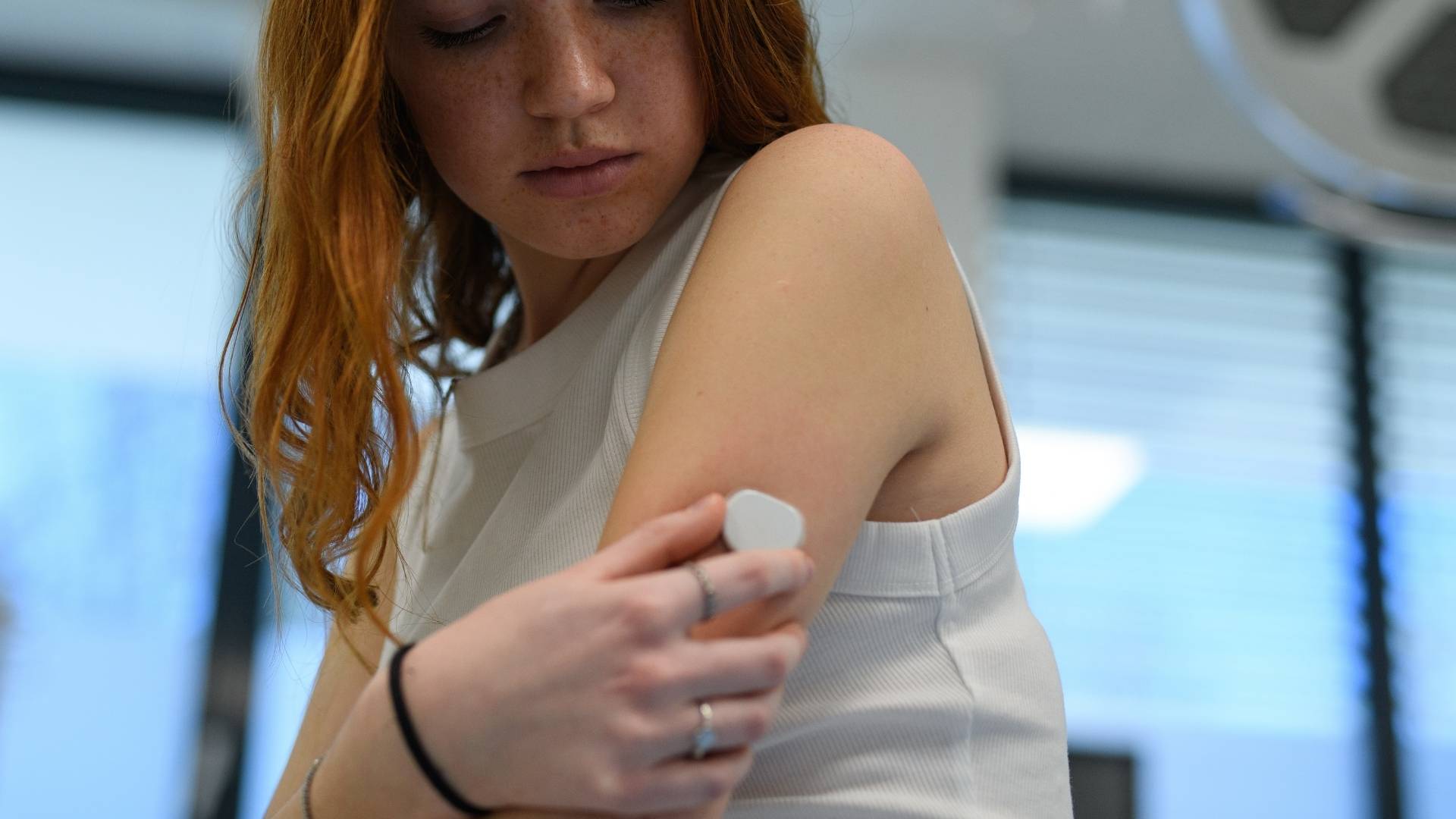A young woman wears a continuous glucose monitor on her arm