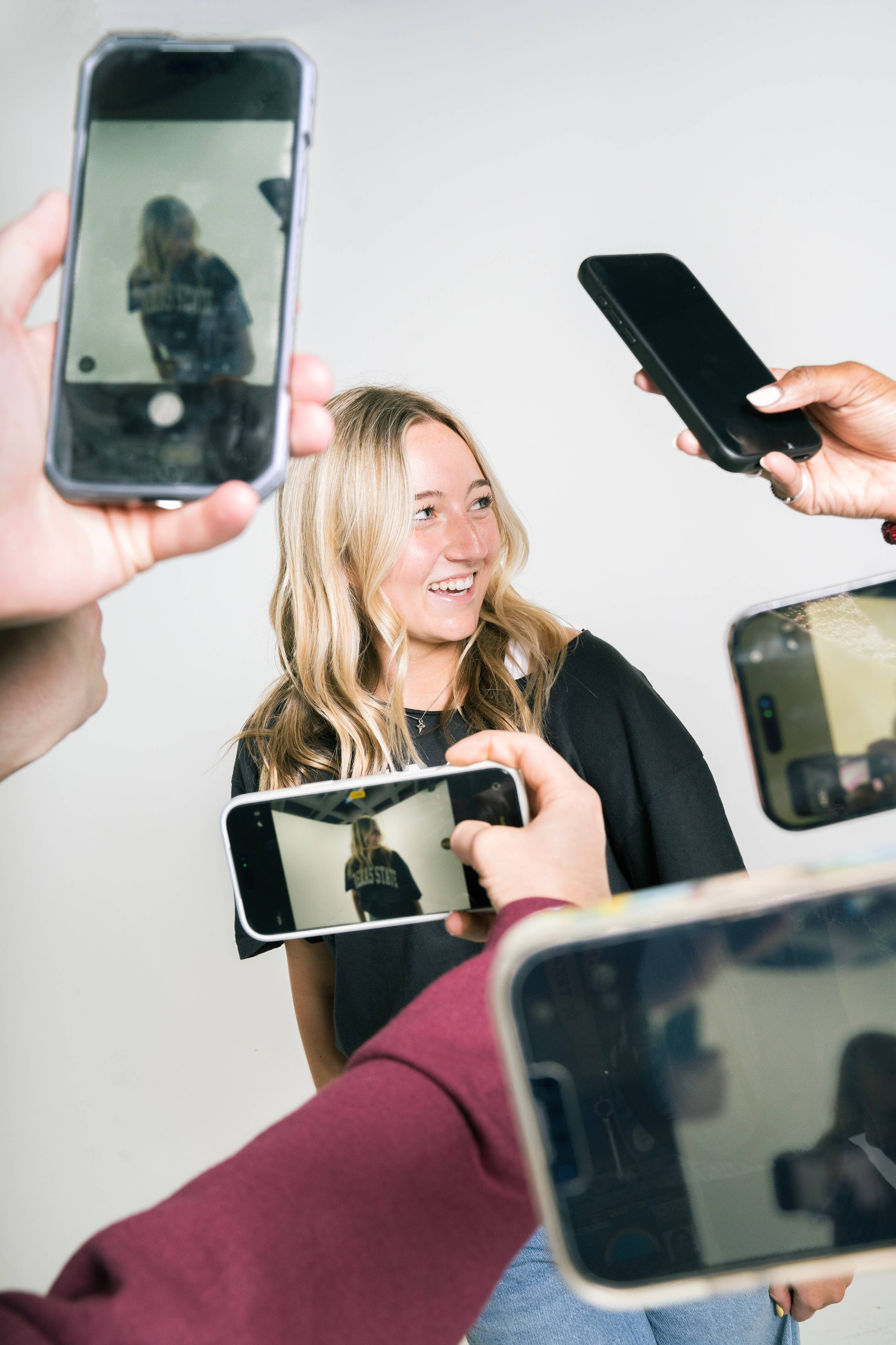 woman smiles while give other people hold up iphones to take photo of her