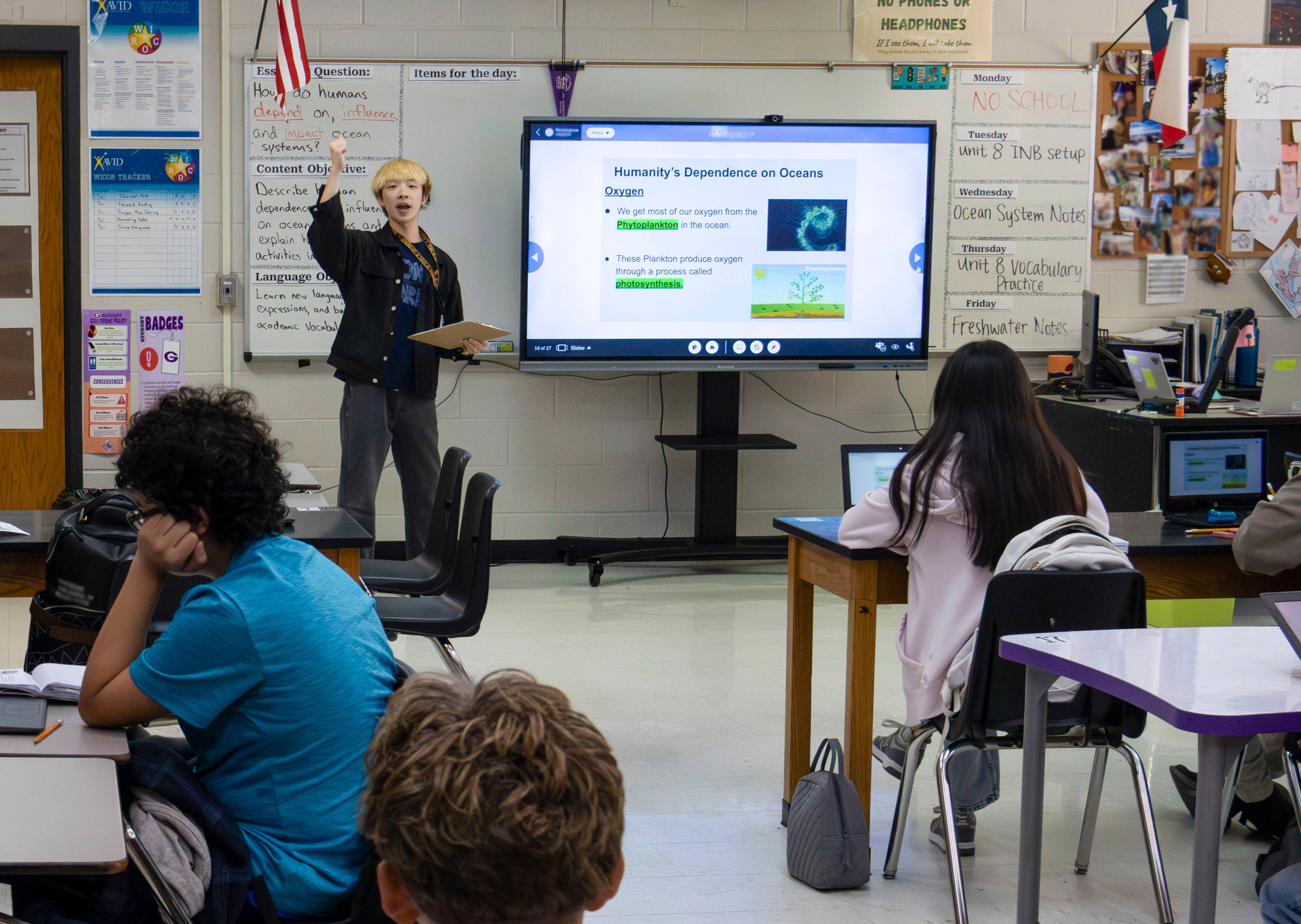 young man speaks in front of a classroom of students