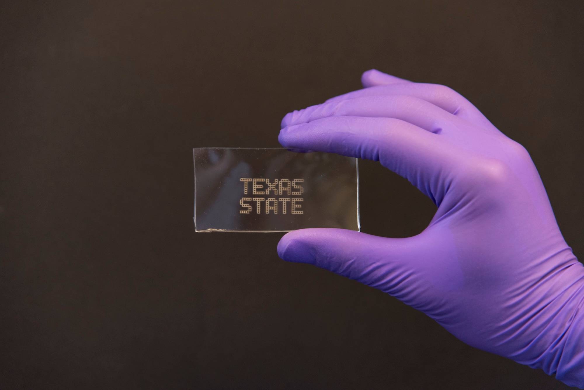 Hand with a glove holding Texas State logo printed on lab equipmenr