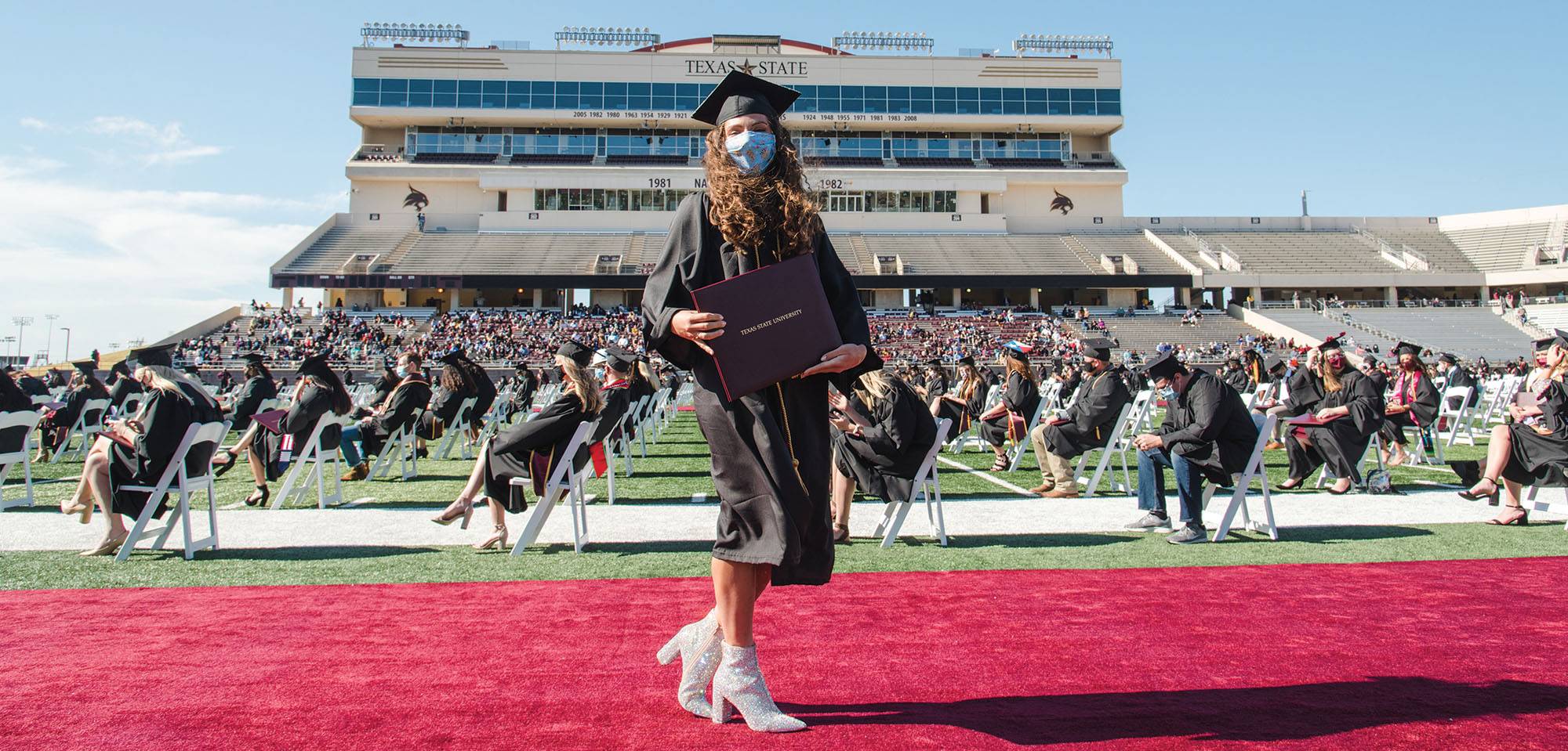 Student at commencement on the football field wearing a face mask
