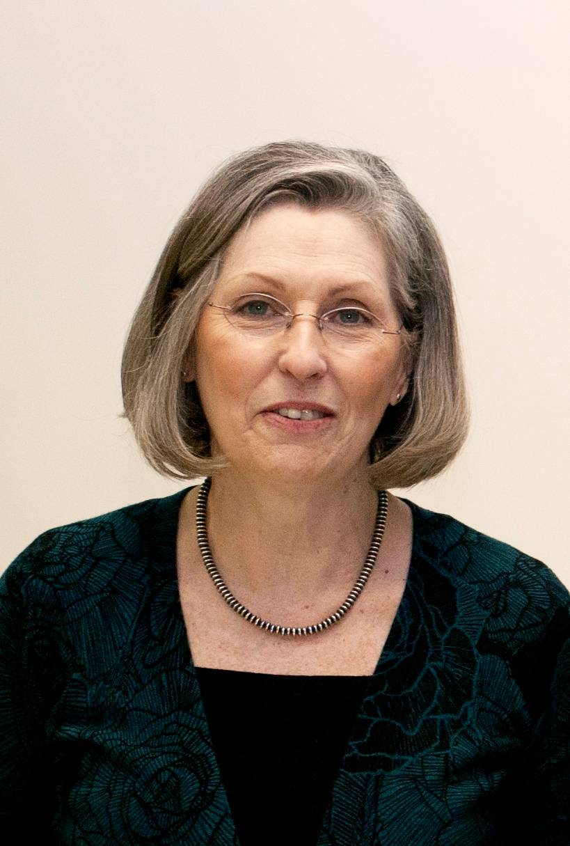 woman with grey hair and black shirt smiling before a white back ground