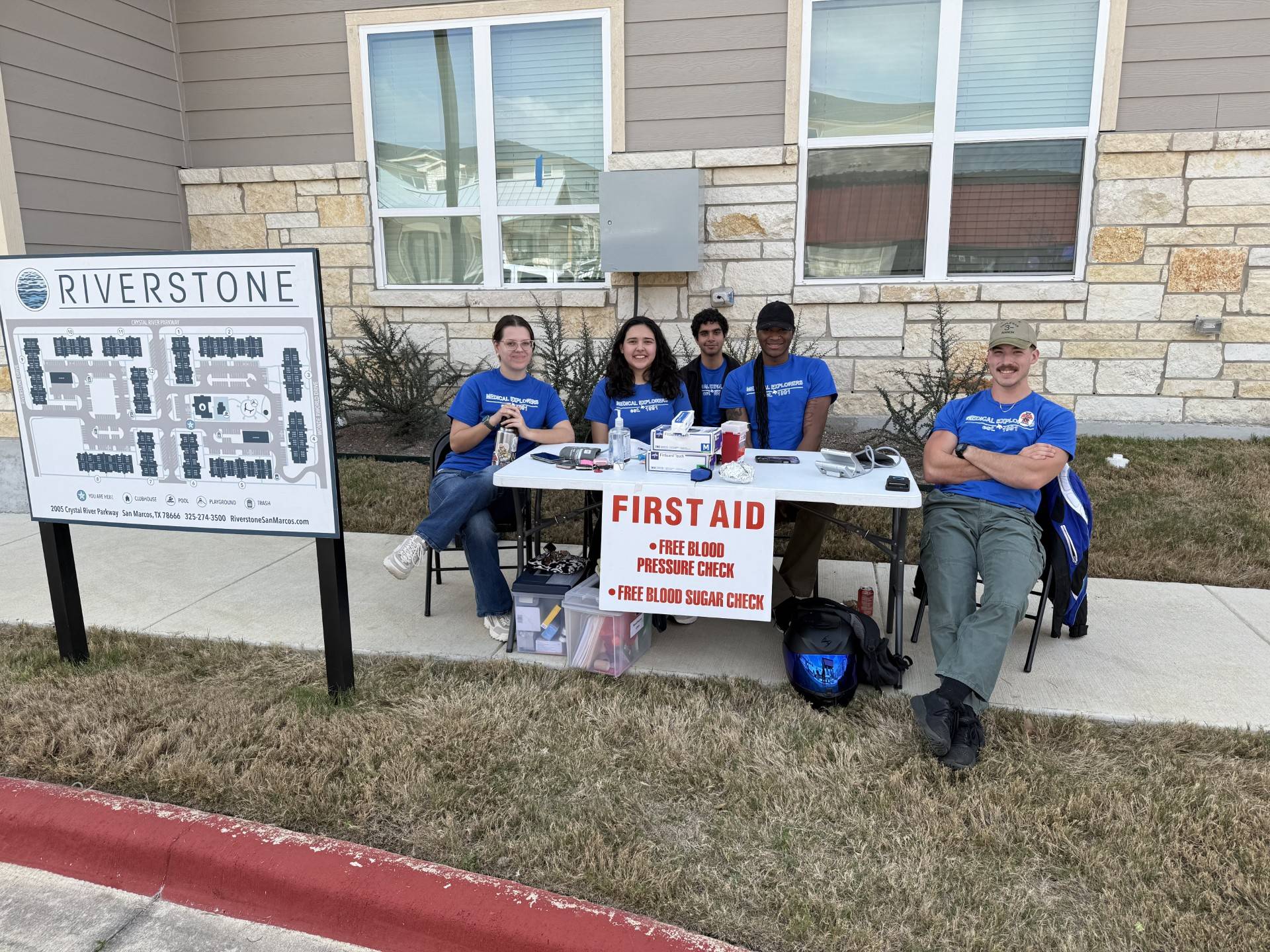 five people in royal blue shirts sit at a table that reads "first aid"