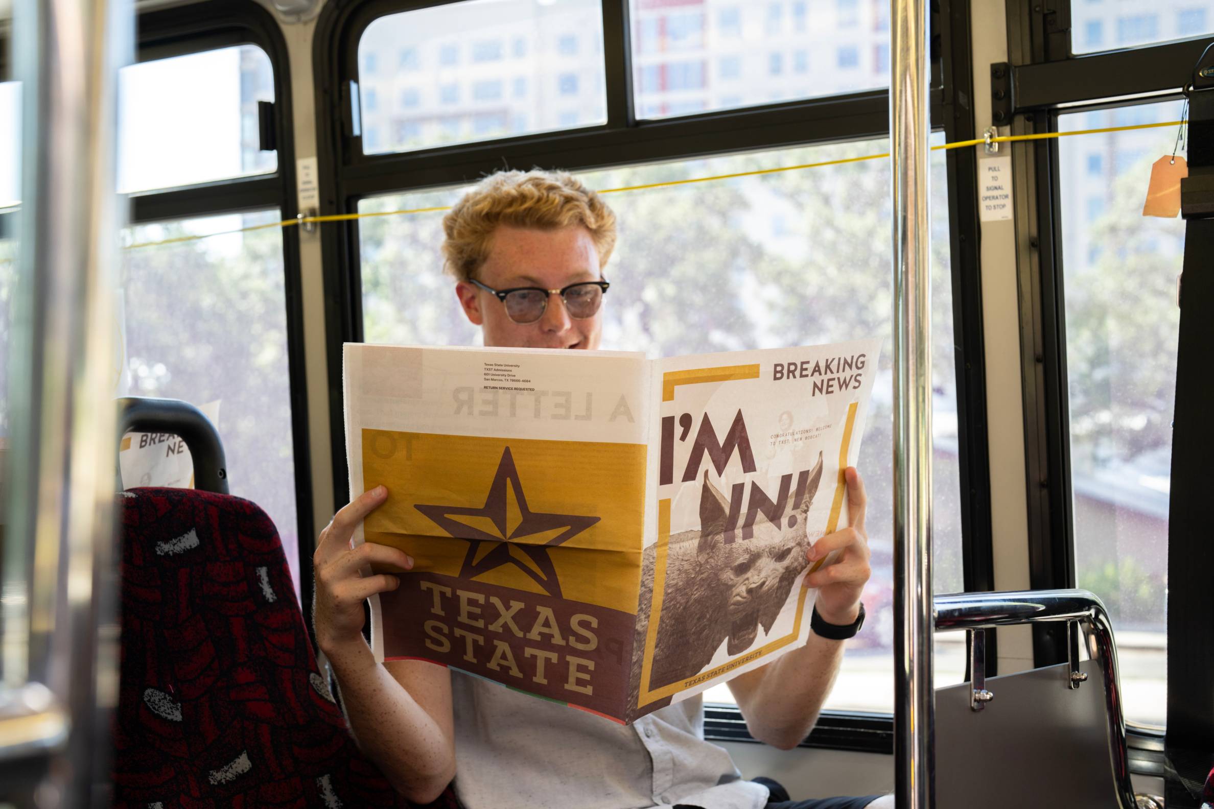 man sitting in bus reading a newspaper that reads "I'm in!"