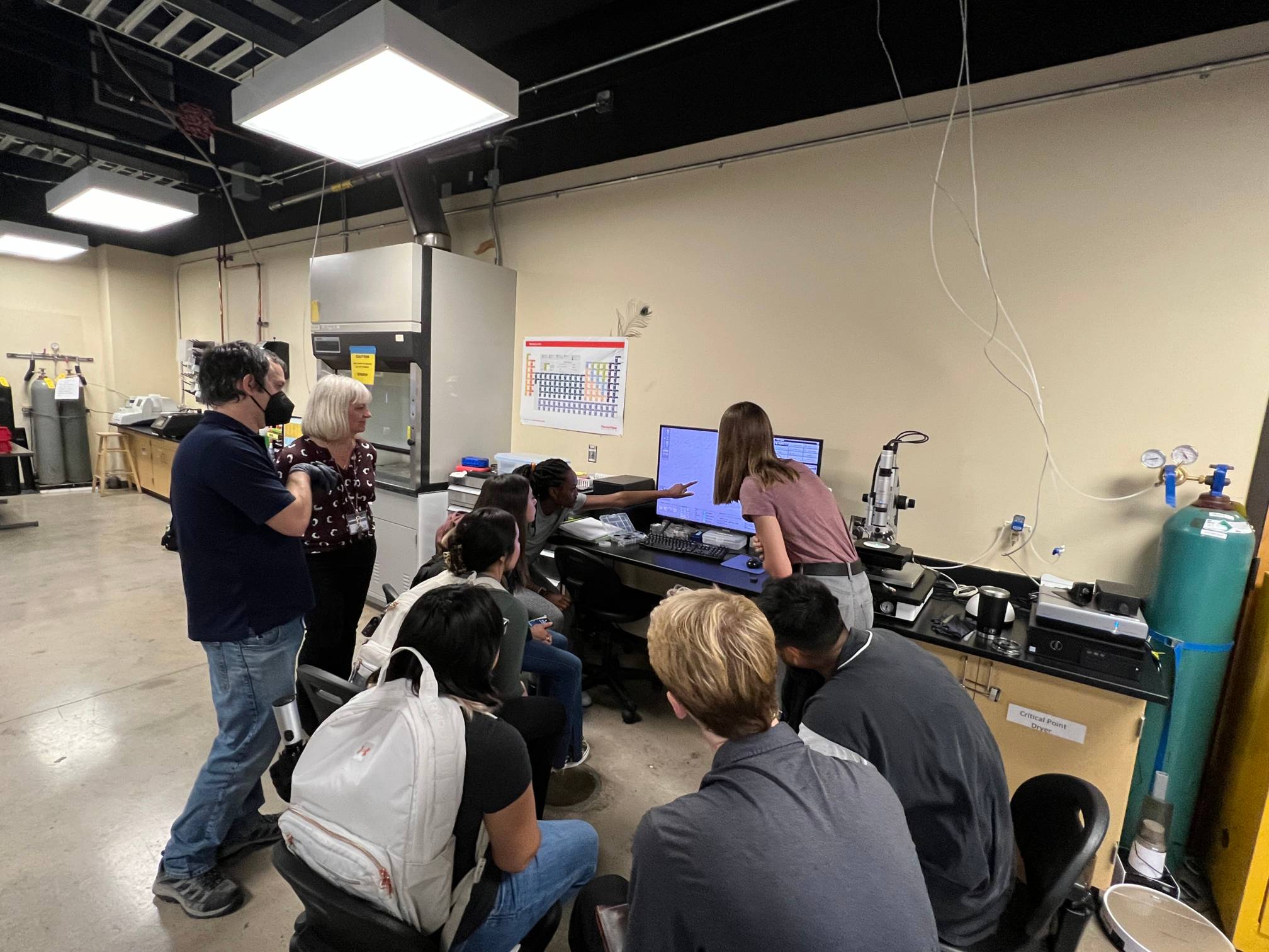 Students and staff gathered around lab equipment receiving hands-on research training.