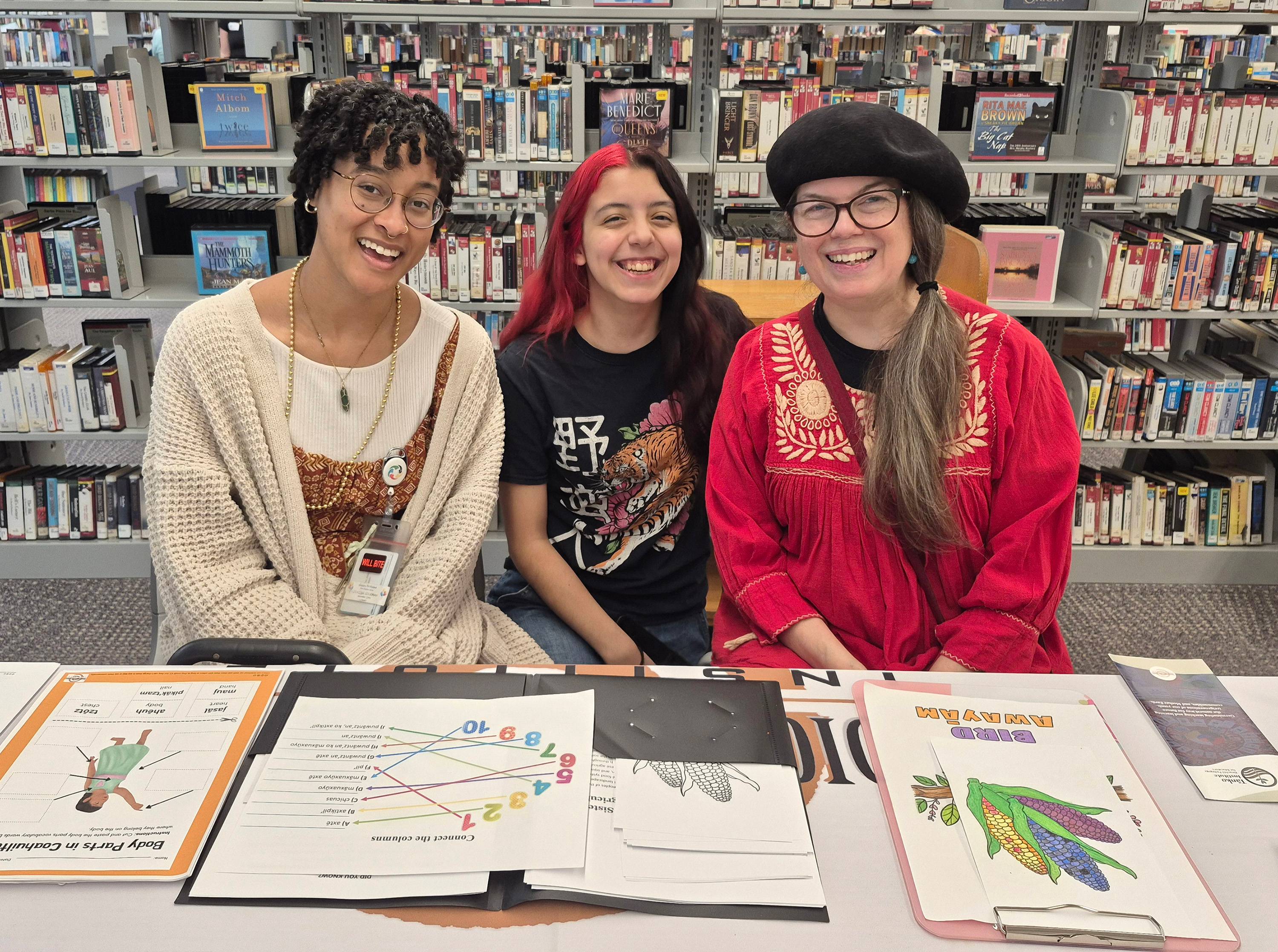 three women sitting behind a table and smiling at camera