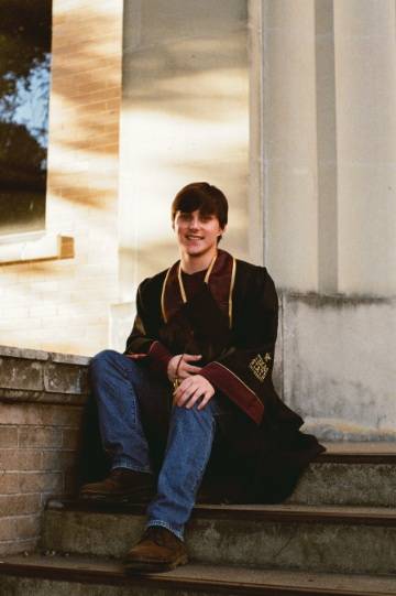 man sitting on steps of building wearing graduation regalia
