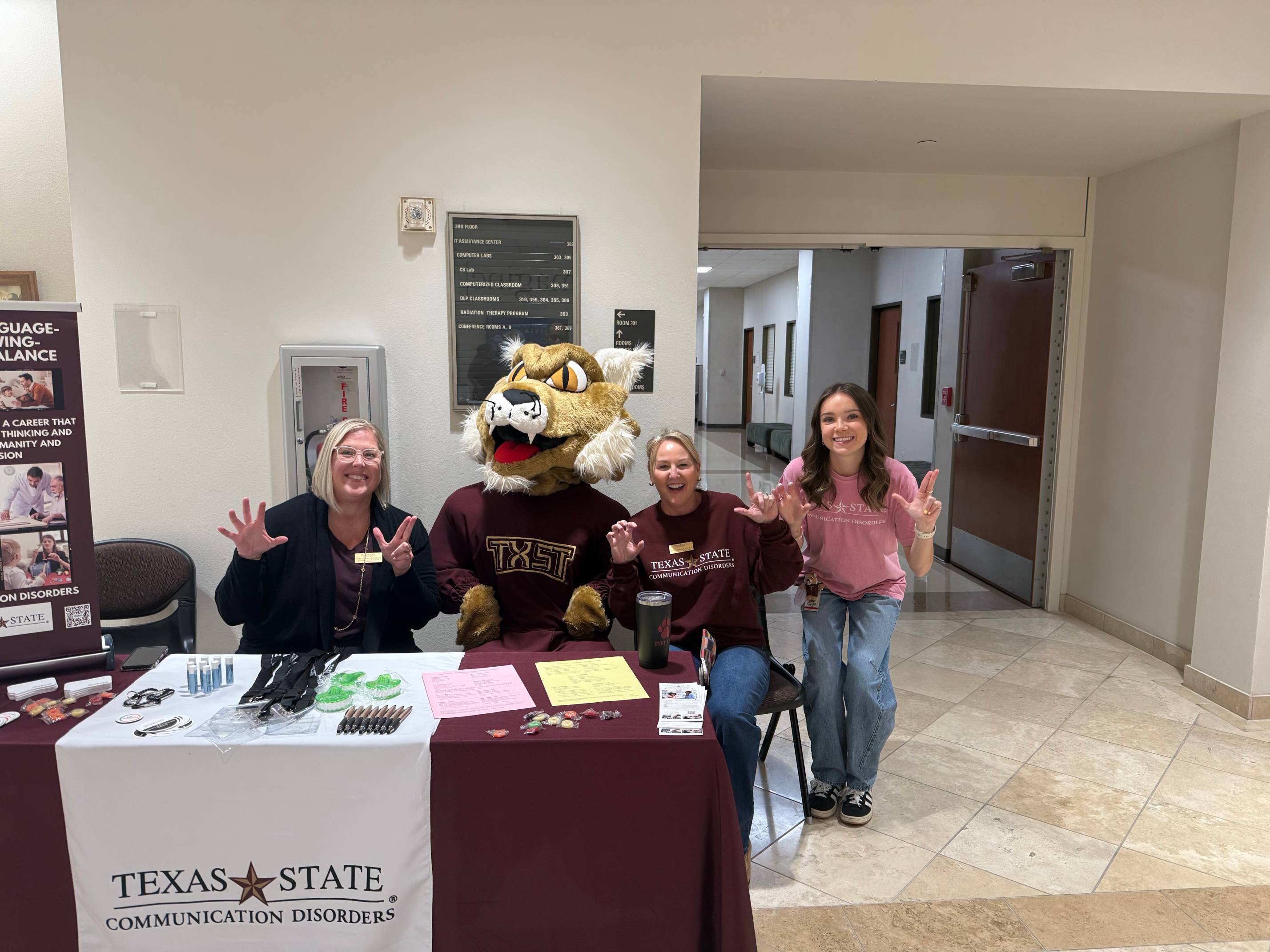 Ms. Beth Rasmussen, Ms. Stacey Lesieur, a CDIS student, and Boko sitting at a booth during the event.