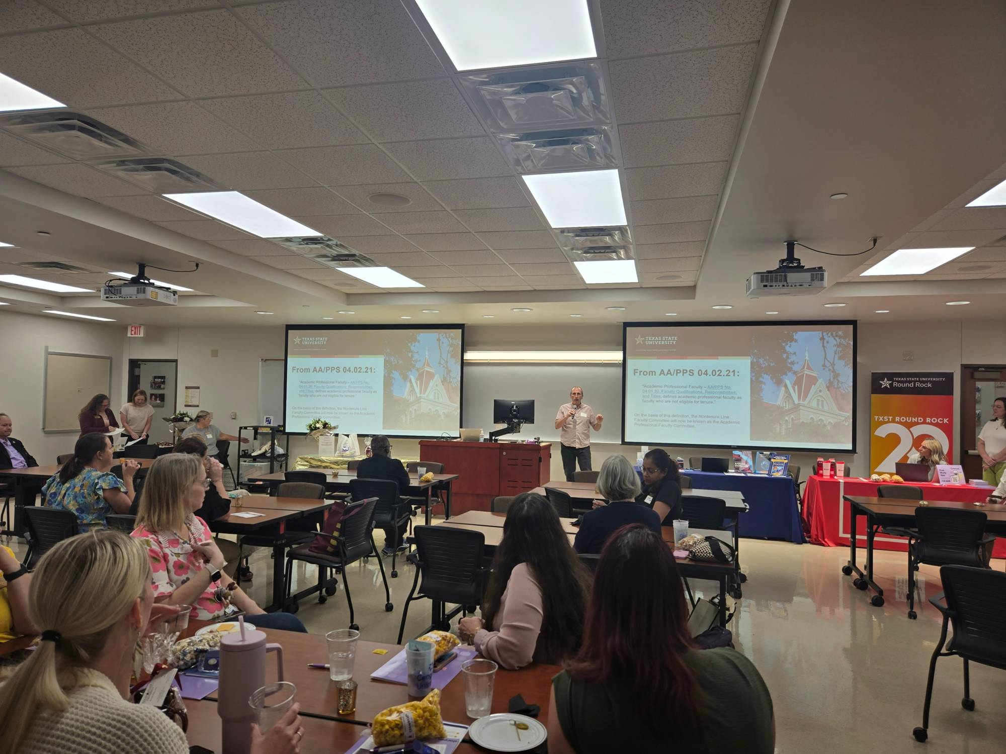 Wide view of faculty gathered for the luncheon, engaged in a presentation highlighting campus initiatives and achievements.