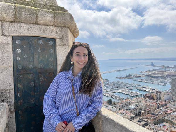 woman with long hair and blue pinstriped shirt, Castillo de Santa Bárbara (Santa Barbara Castle) in Alicante, Spain in background