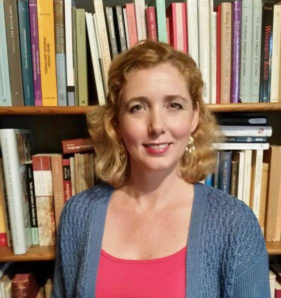 woman wearing blue cardigan and salmon top, standing in front of bookshelf