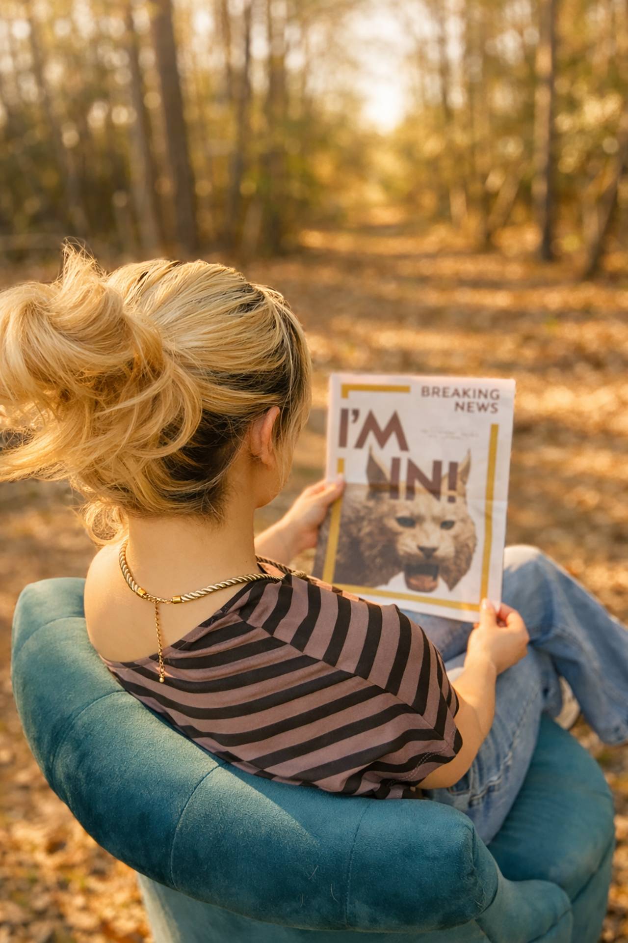 back of woman who is sitting in teal chair. she is looking at a newspaper reading "I'm in!"