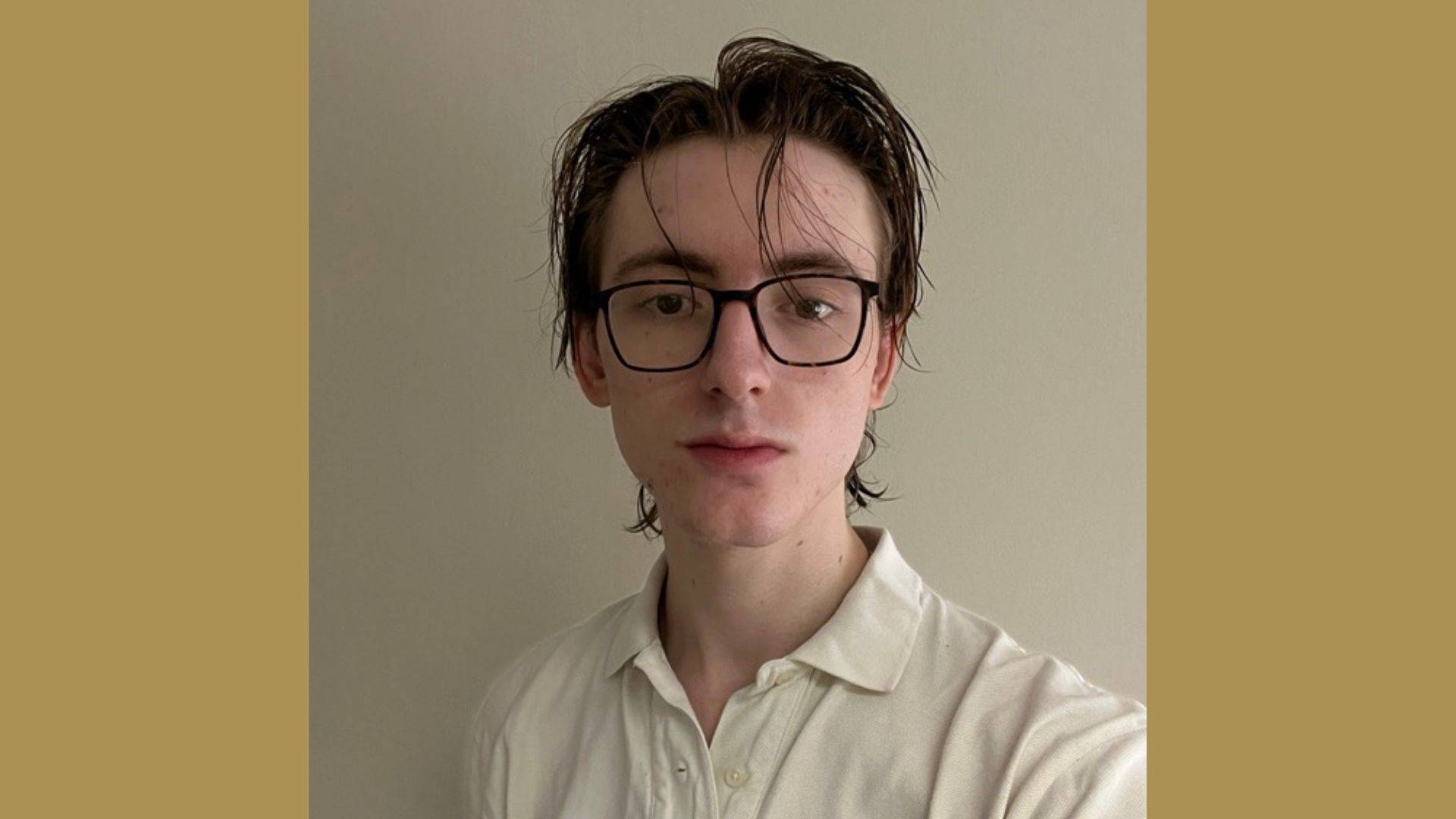 young man with glasses and white polo in front of beige wall