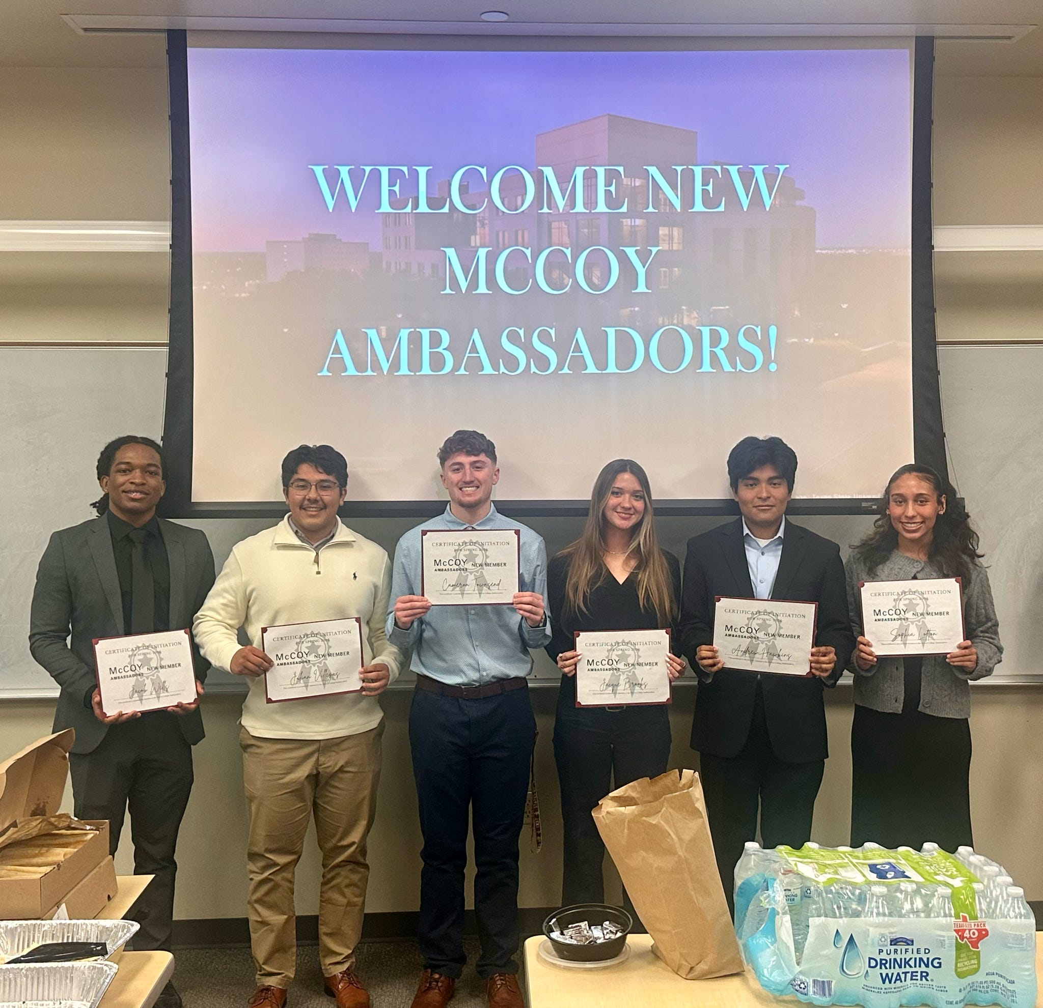Six newly initiated McCoy Ambassadors standing in front of a screen that says "Welcome New McCoy Ambassadors"