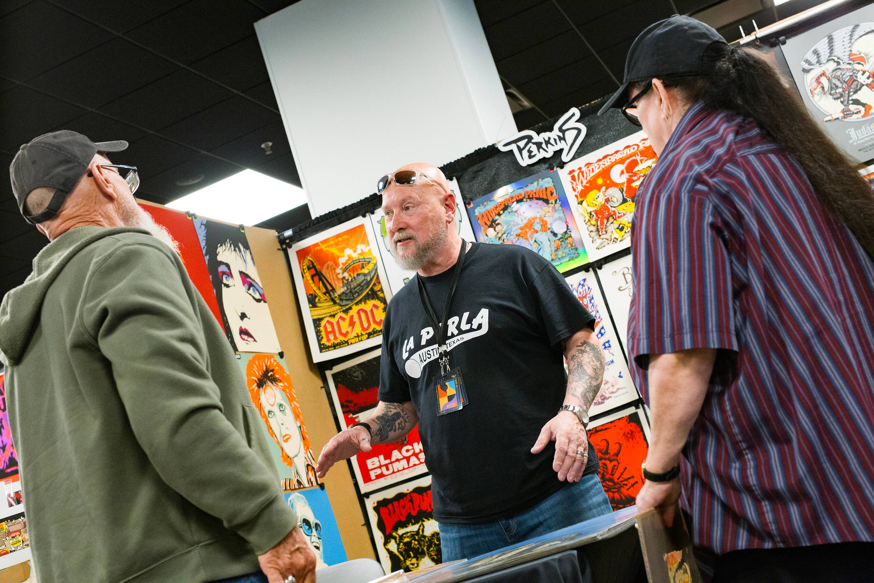 Artist speaking with two people visiting his booth filled with colorful art. 