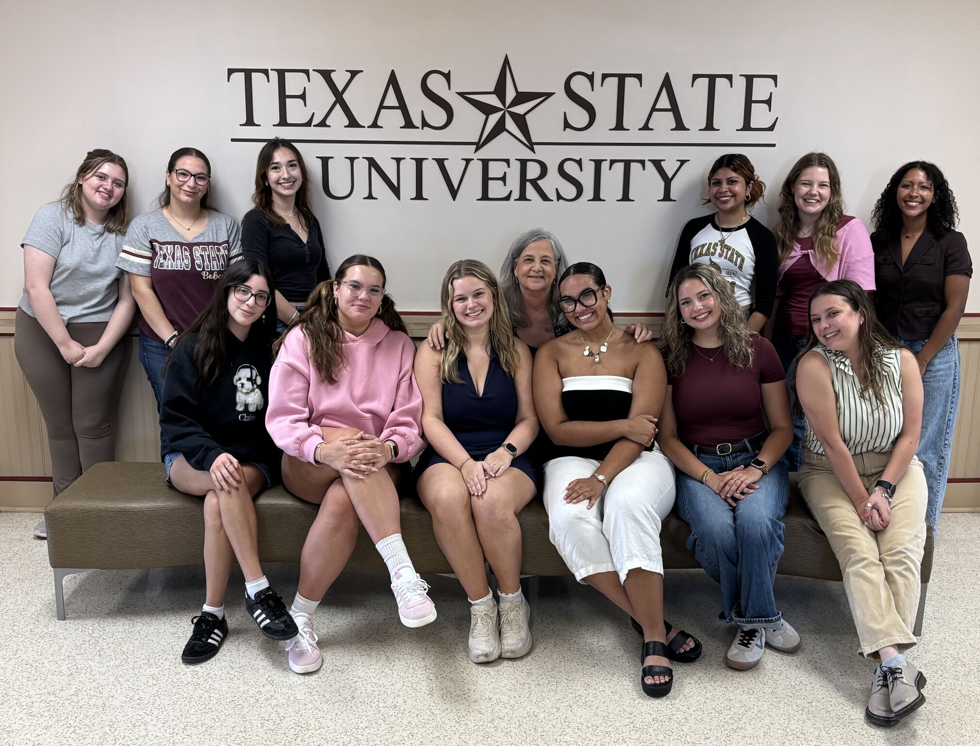 large group photo of women in front of Texas State University sign