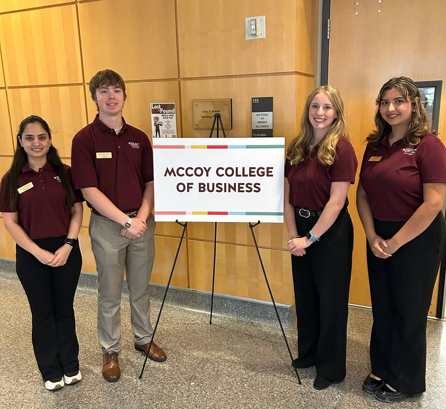Four McCoy Ambassadors at Bobcat Day presentations, standing with a sign that says "McCoy College of Business"